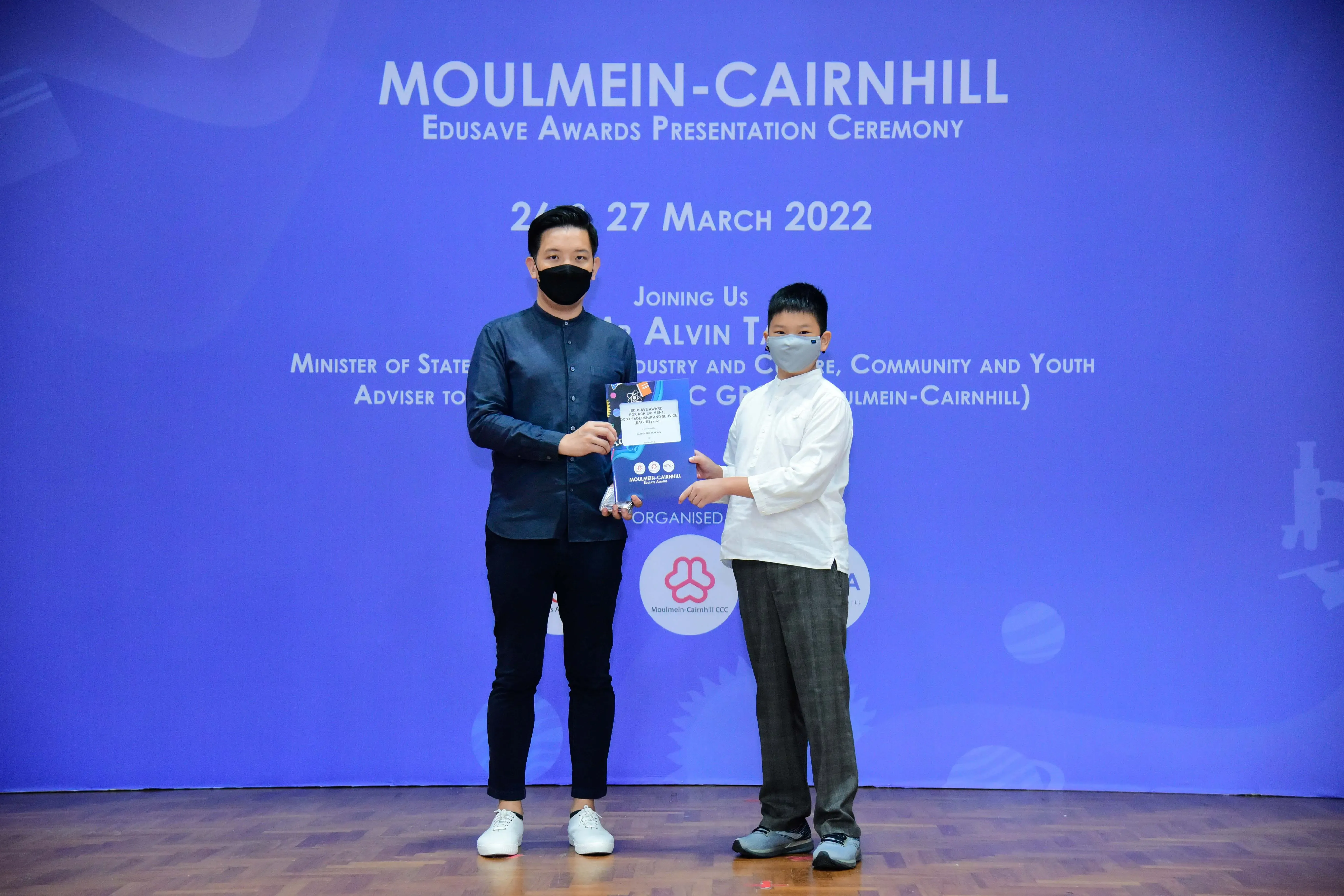 An adult and a child wearing masks hold an award together at the Moulmein-Cairnhill Edusave Awards Ceremony, March 2022.