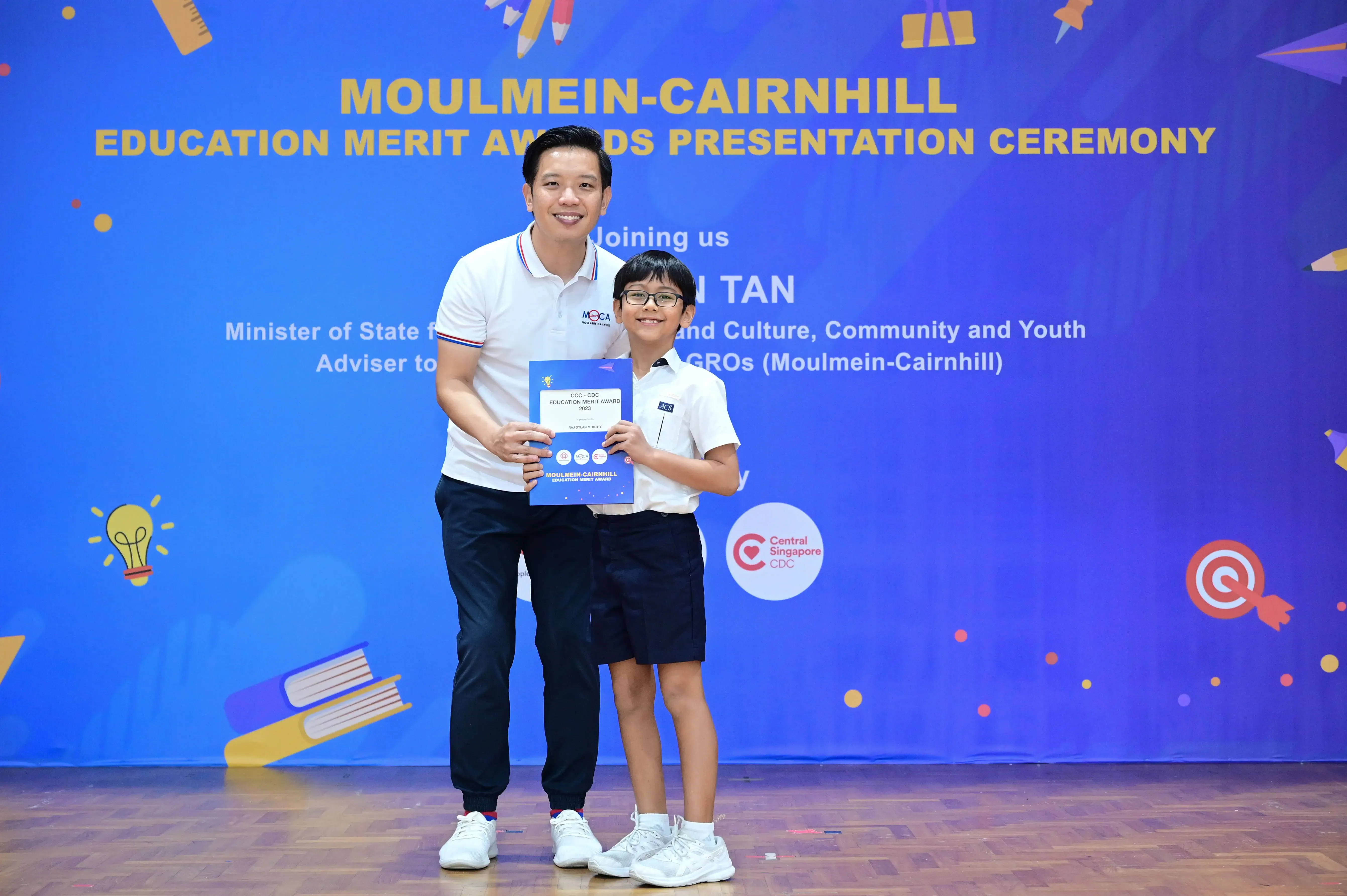 A man and a young boy hold an award certificate at the Moulmein-Cairnhill Education Merit Awards Presentation Ceremony.