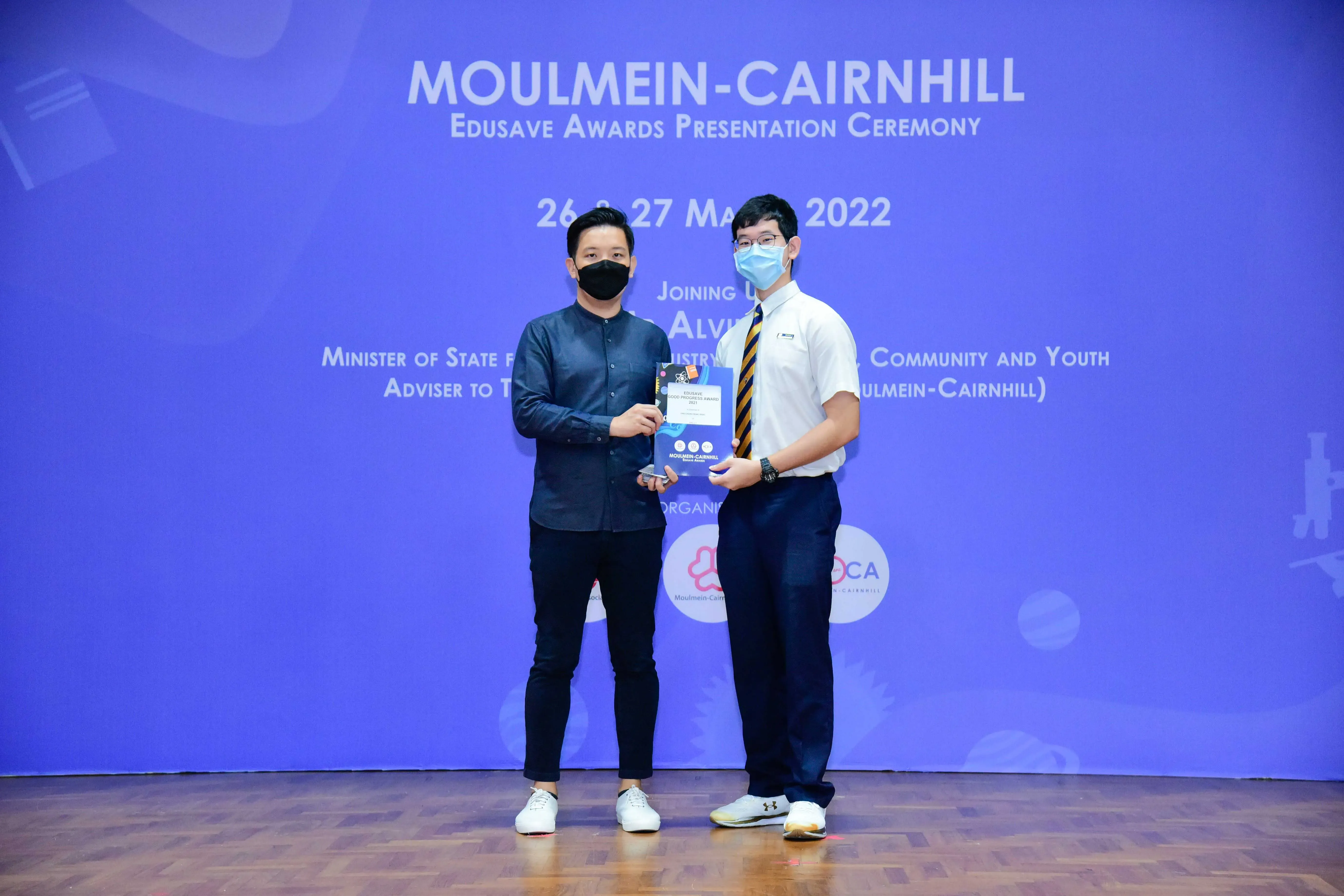 Two masked men hold a certificate at the Moulmein-Cairnhill Edusave Awards Presentation Ceremony, March 2022.