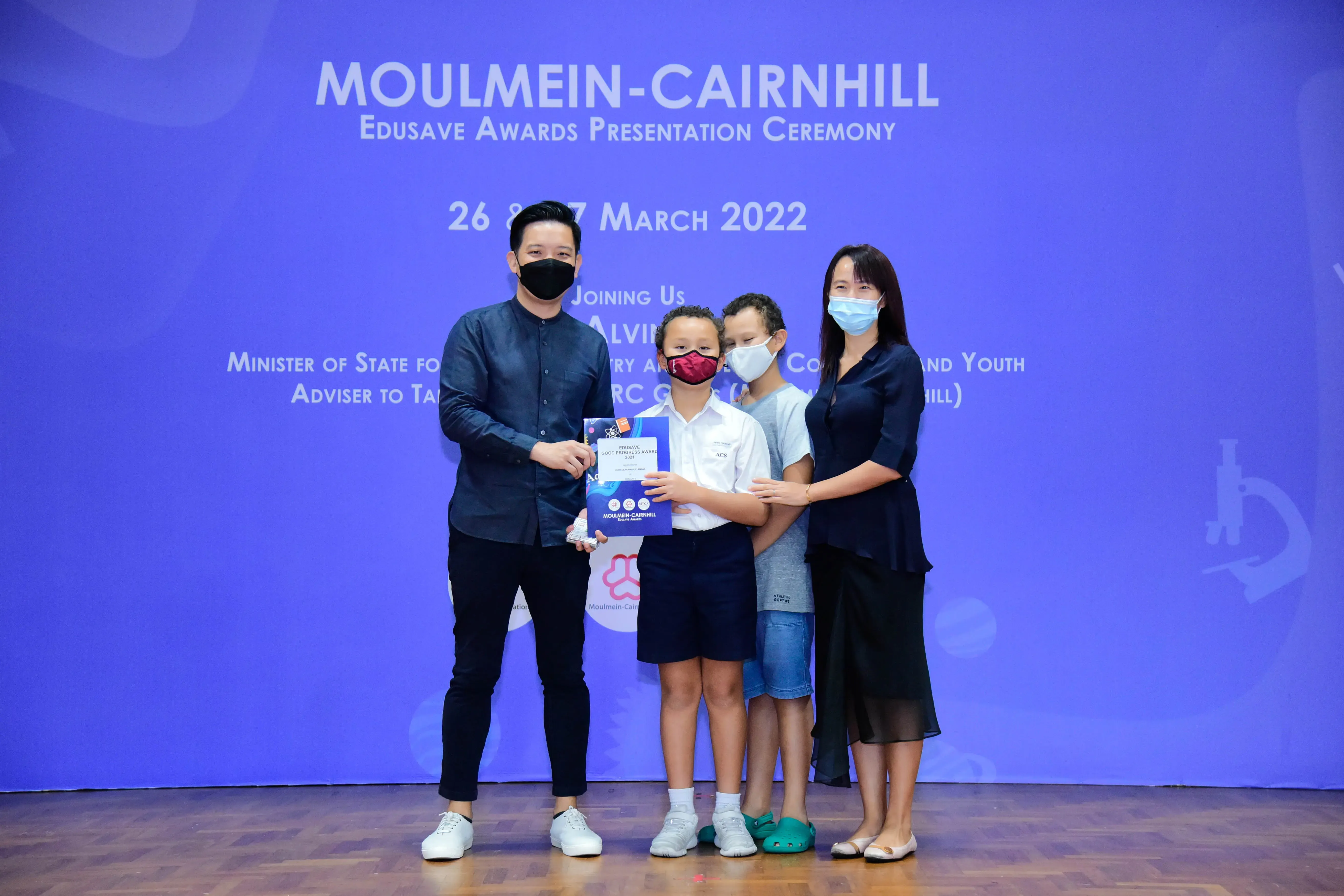 Four masked people pose with an award certificate at the Moulmein-Cairnhill Edusave Awards Ceremony, March 2022.