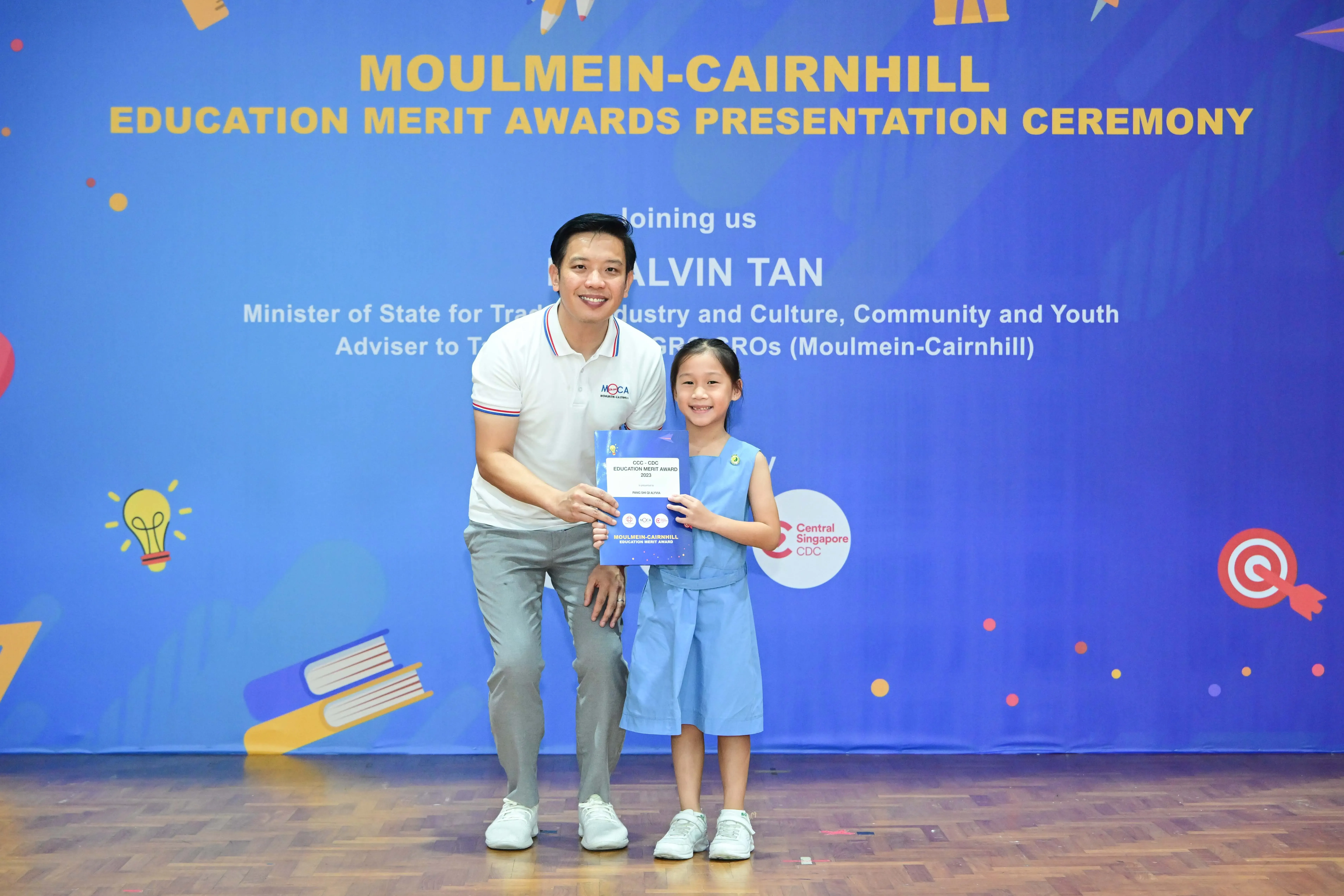 A man and a young girl hold a certificate at the Moulmein-Cairnhill Education Merit Awards Presentation Ceremony.