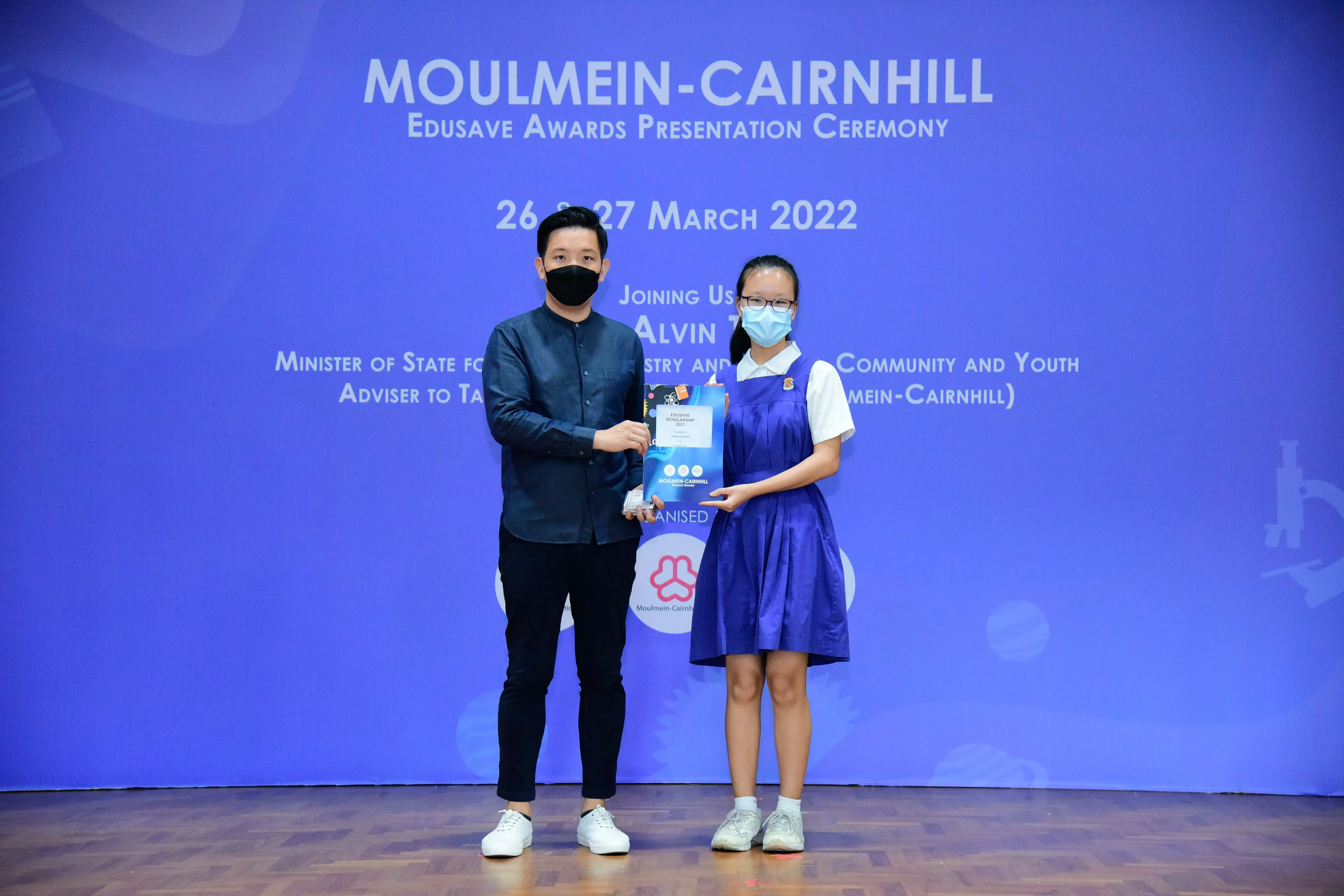 A man and a young girl in school uniform hold an award together at the Moulmein-Cairnhill Edusave Awards Ceremony.