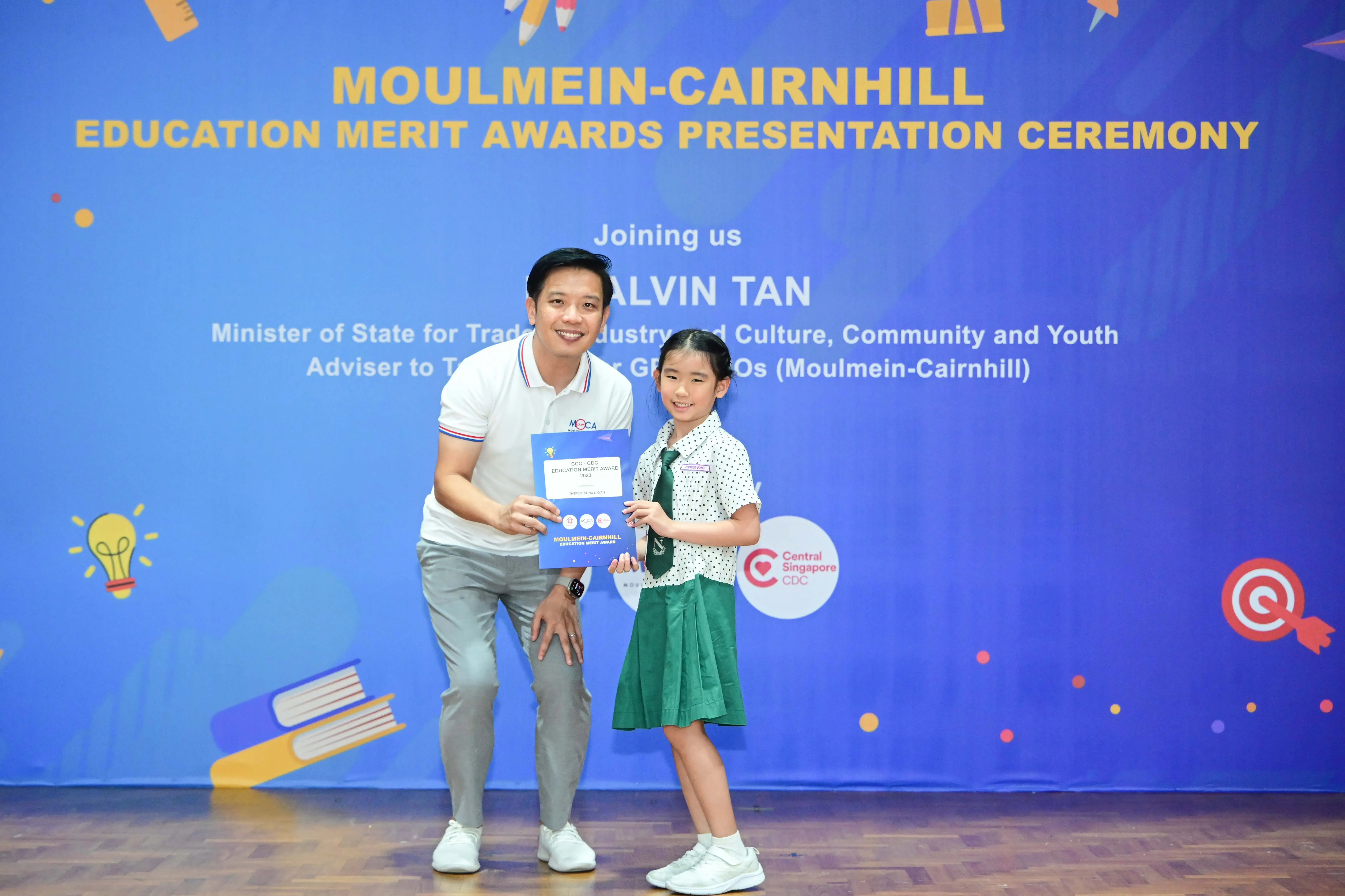 A man and a young girl in school uniform hold an award certificate at the Moulmein-Cairnhill Education Merit Awards ceremony.