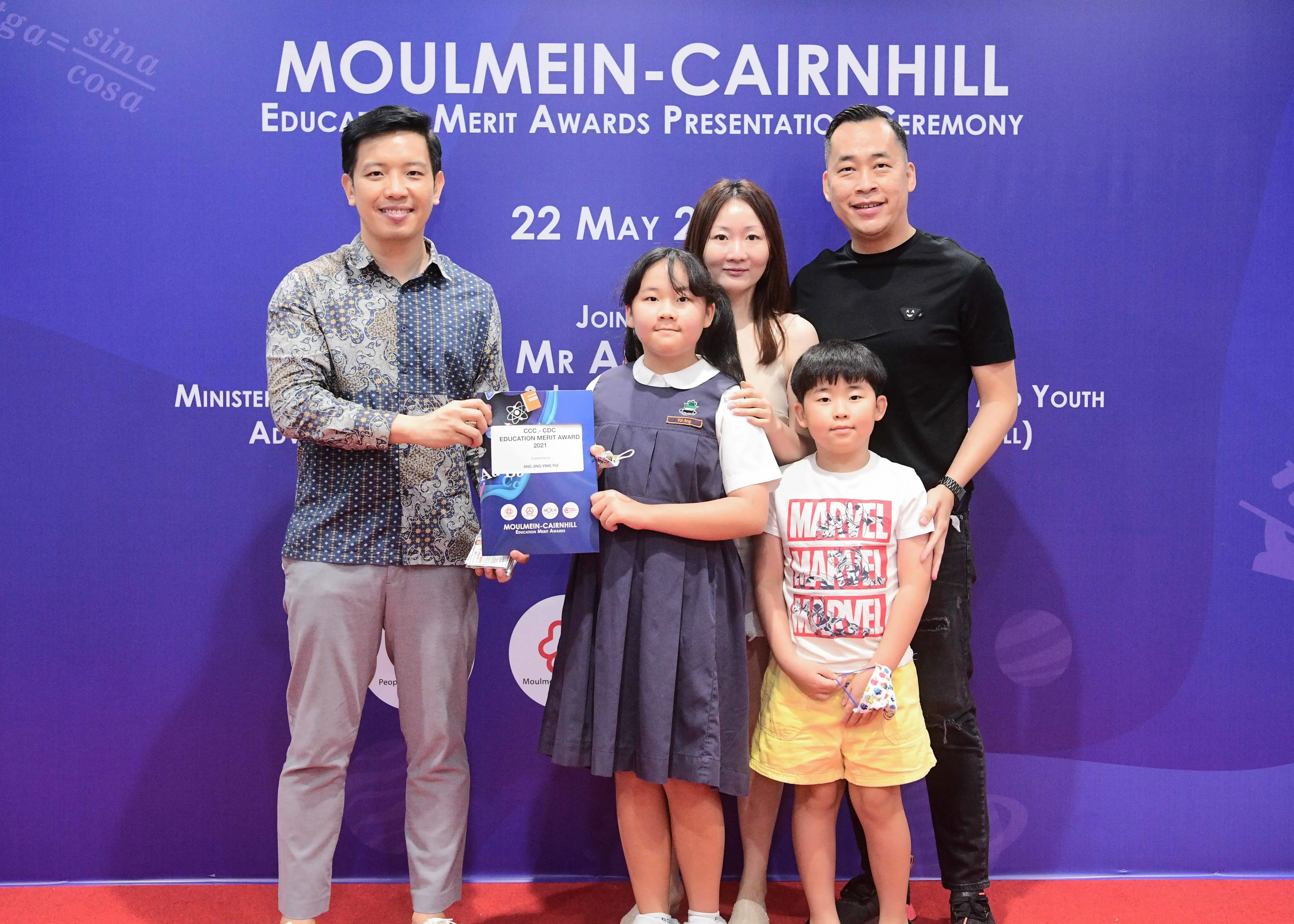 Five people pose at the Moulmein-Cairnhill Education Merit Awards Presentation Ceremony, with a girl holding an award certificate.