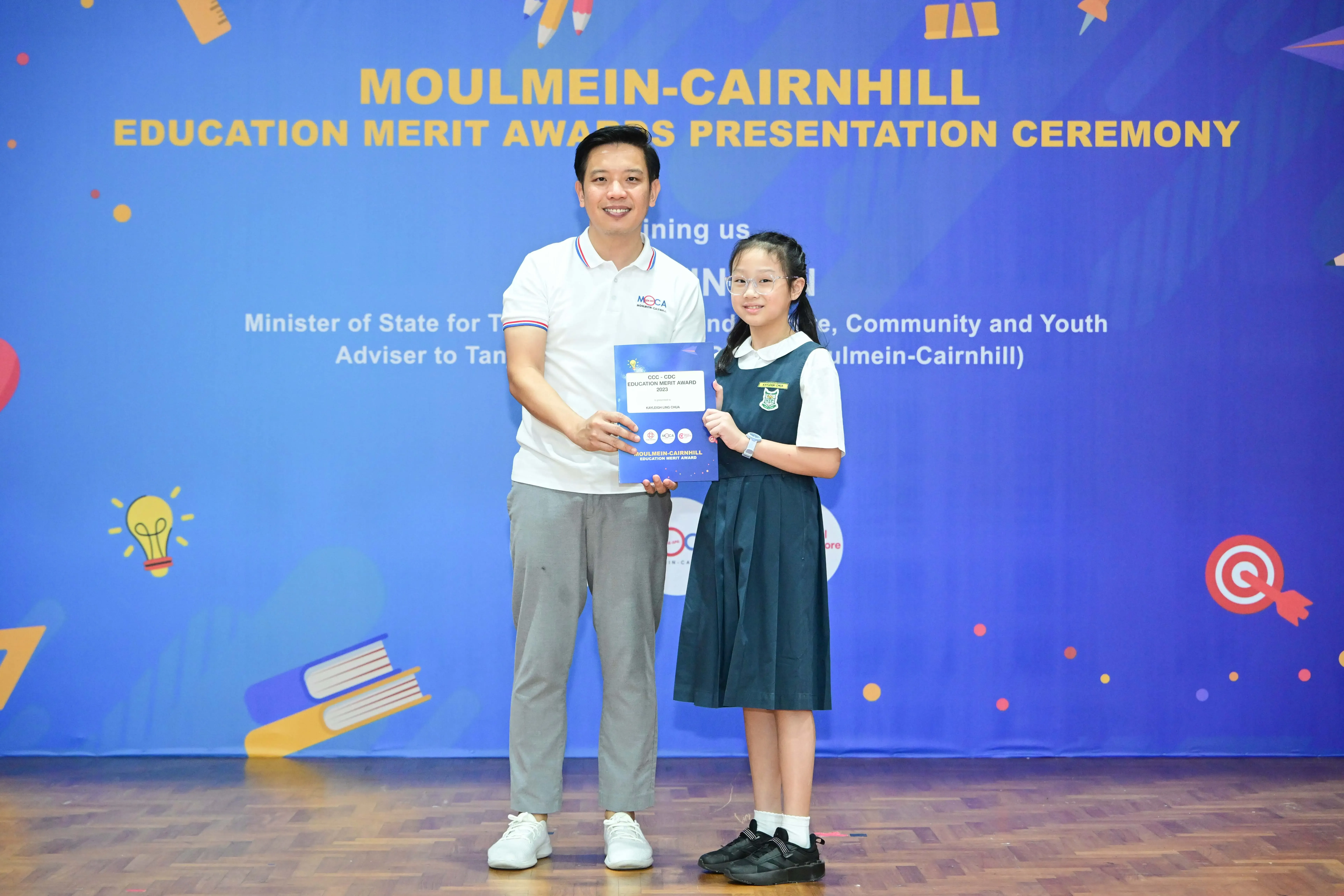 Man and young girl in school uniform hold a certificate at Moulmein-Cairnhill Education Merit Awards ceremony.