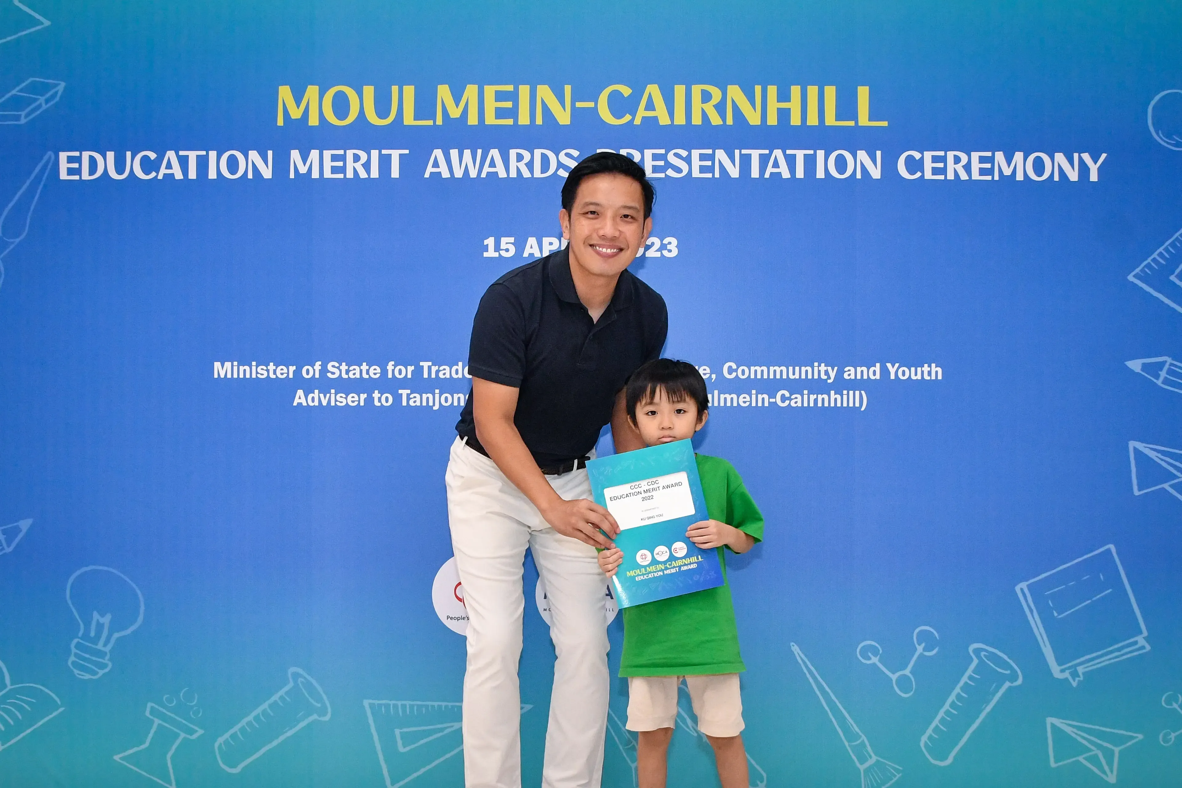 Man and young child pose together holding an award folder at the Moulmein-Cairnhill Education Merit Awards Ceremony.