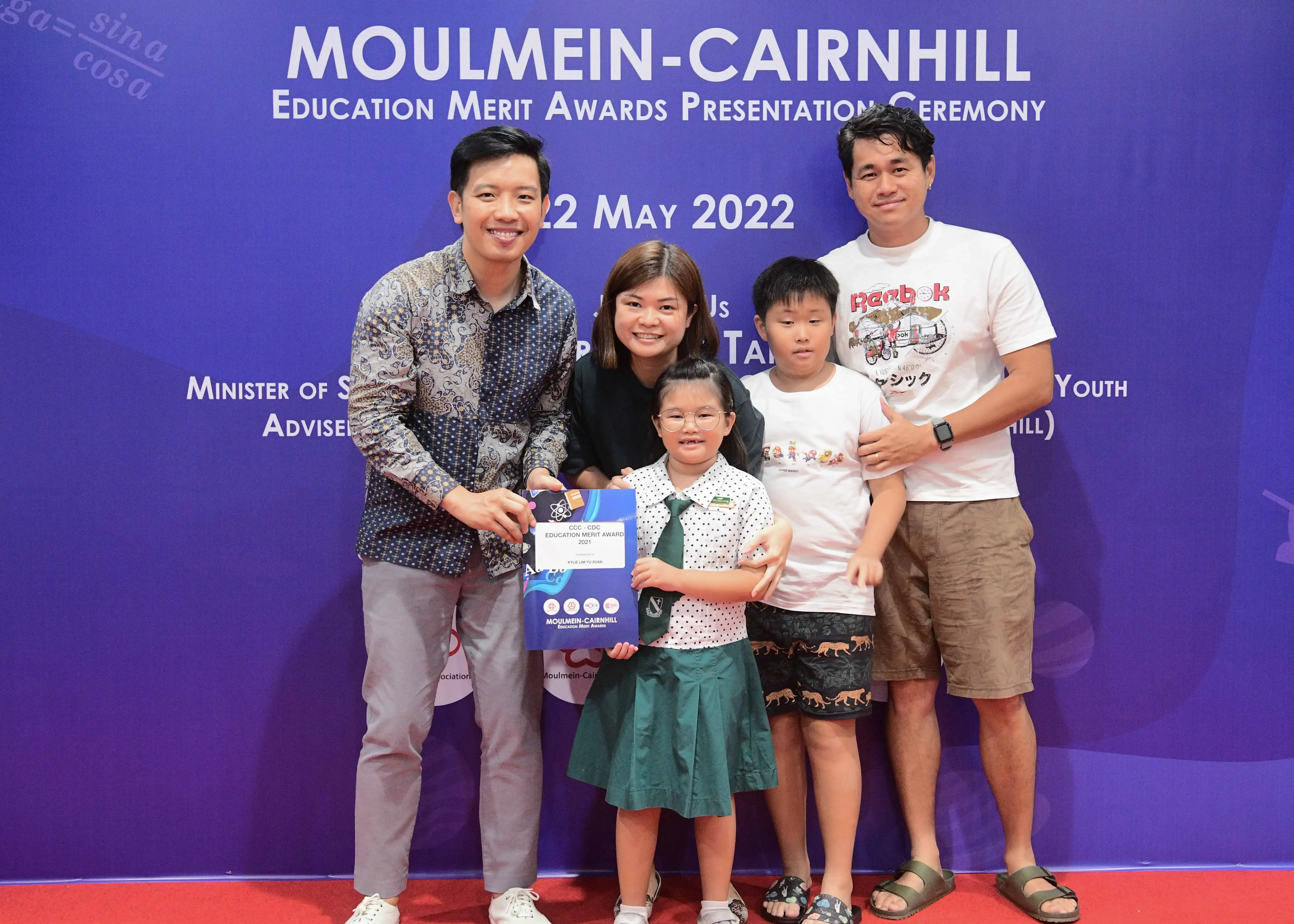 Five people pose at the Moulmein-Cairnhill Education Merit Awards ceremony on 22 May 2022, with a girl holding a certificate.