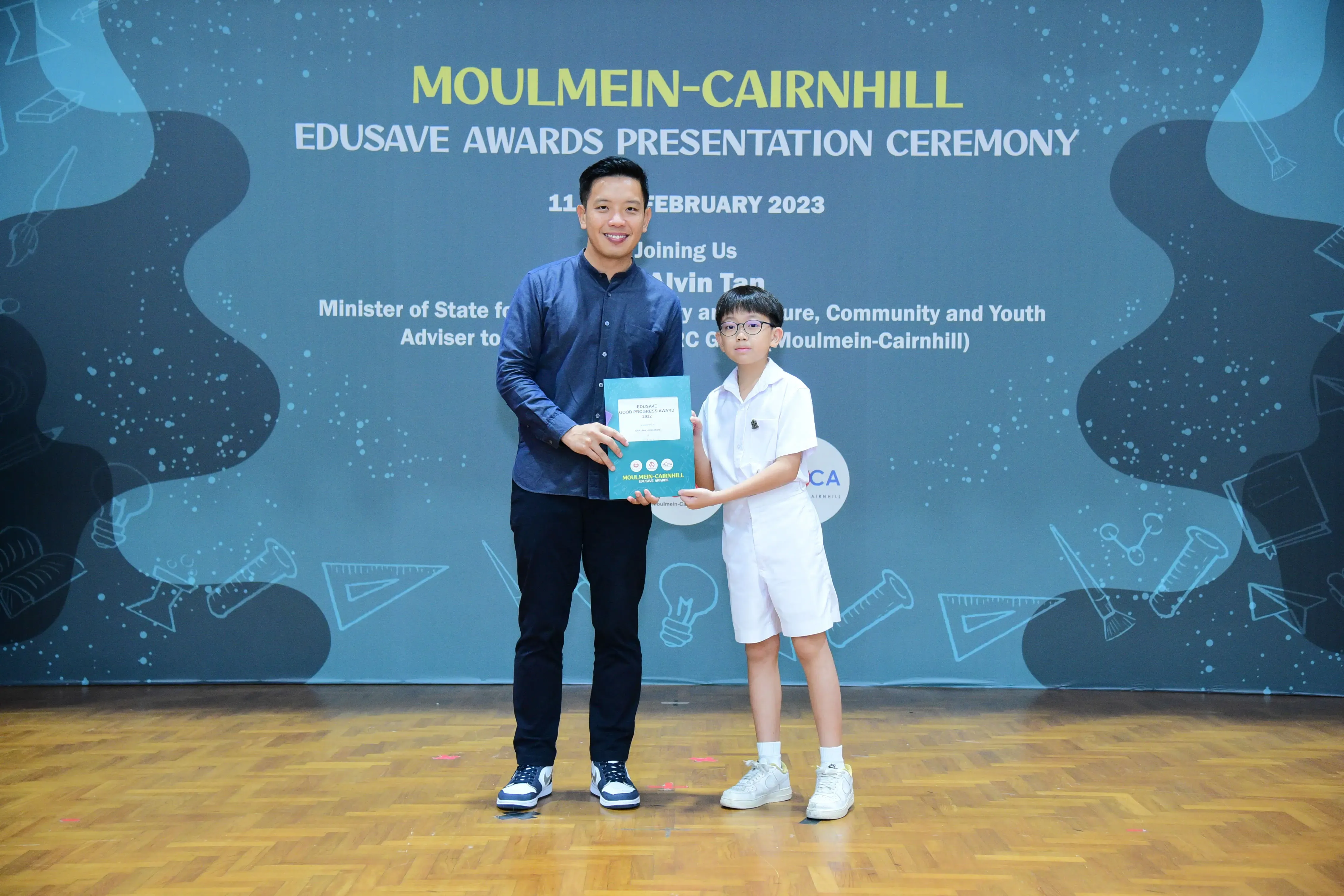 An adult and a young boy hold a certificate together at the Moulmein-Cairnhill Edusave Awards Ceremony, February 2023.