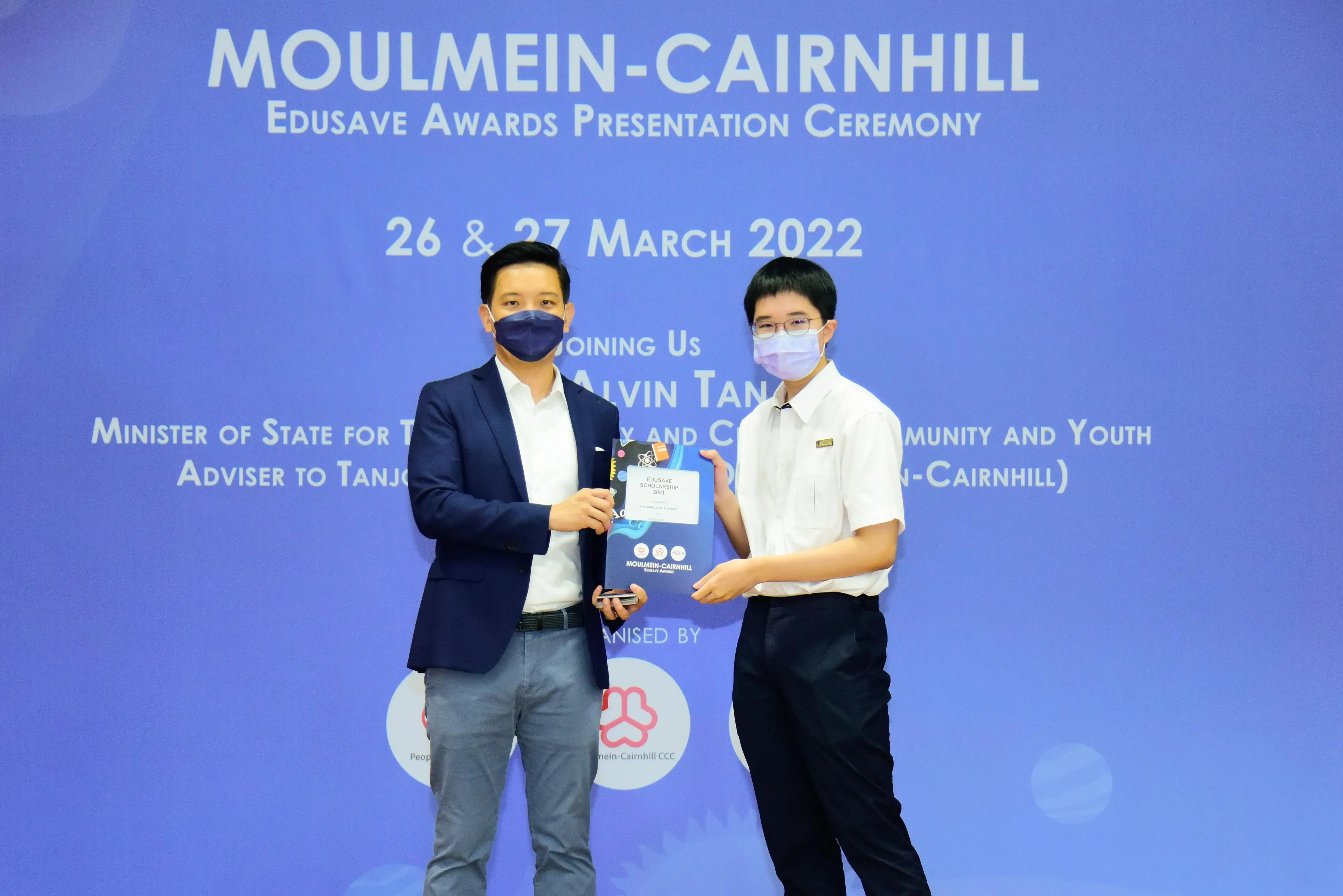 Two masked individuals hold an award at the Moulmein-Cairnhill Edusave Awards Presentation Ceremony, March 2022.