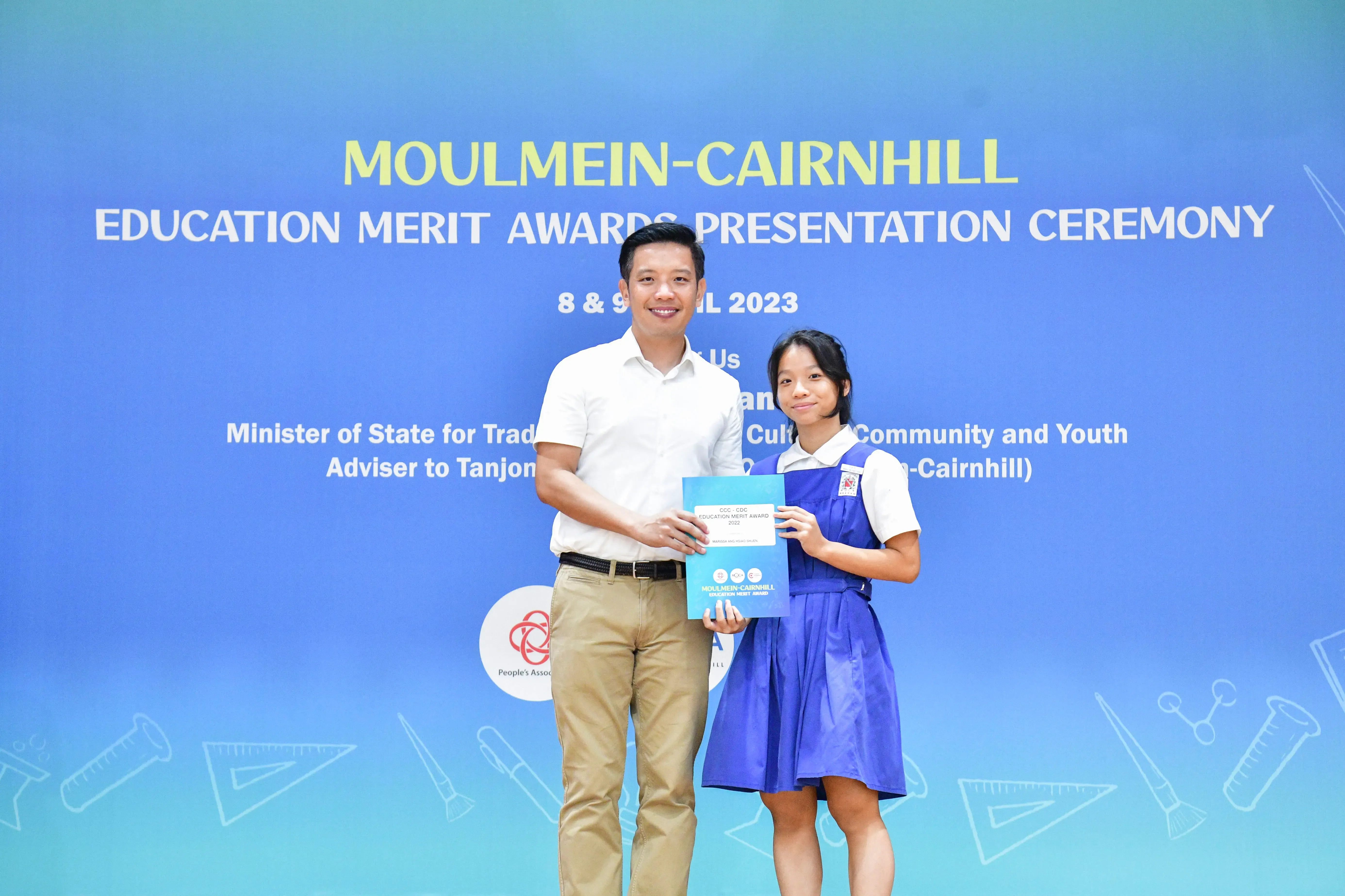 A man and a young girl hold an award certificate at the Moulmein-Cairnhill Education Merit Awards ceremony in 2023.