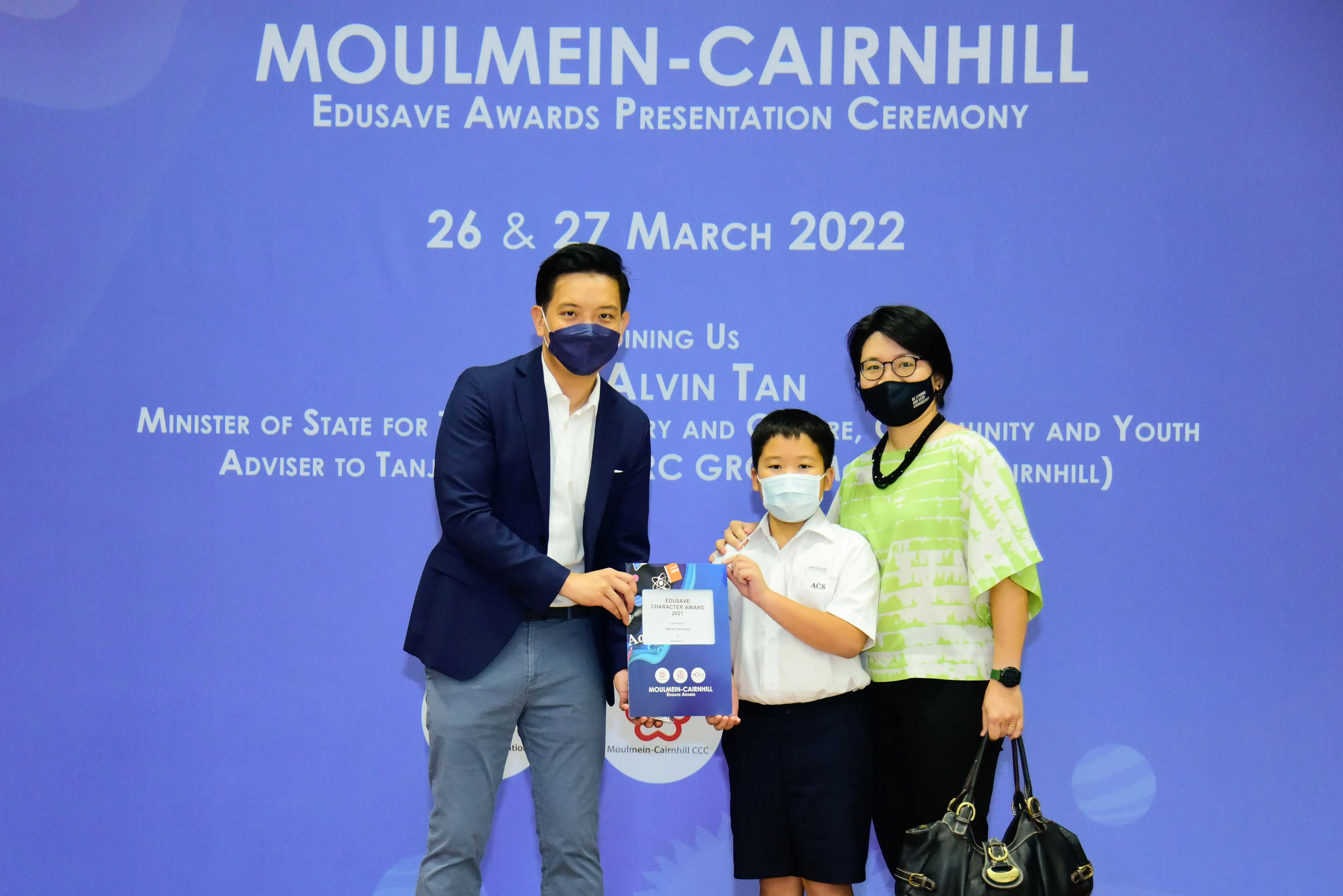 A man, a young boy holding an award certificate, and a woman pose at the Moulmein-Cairnhill Edusave Awards Ceremony.