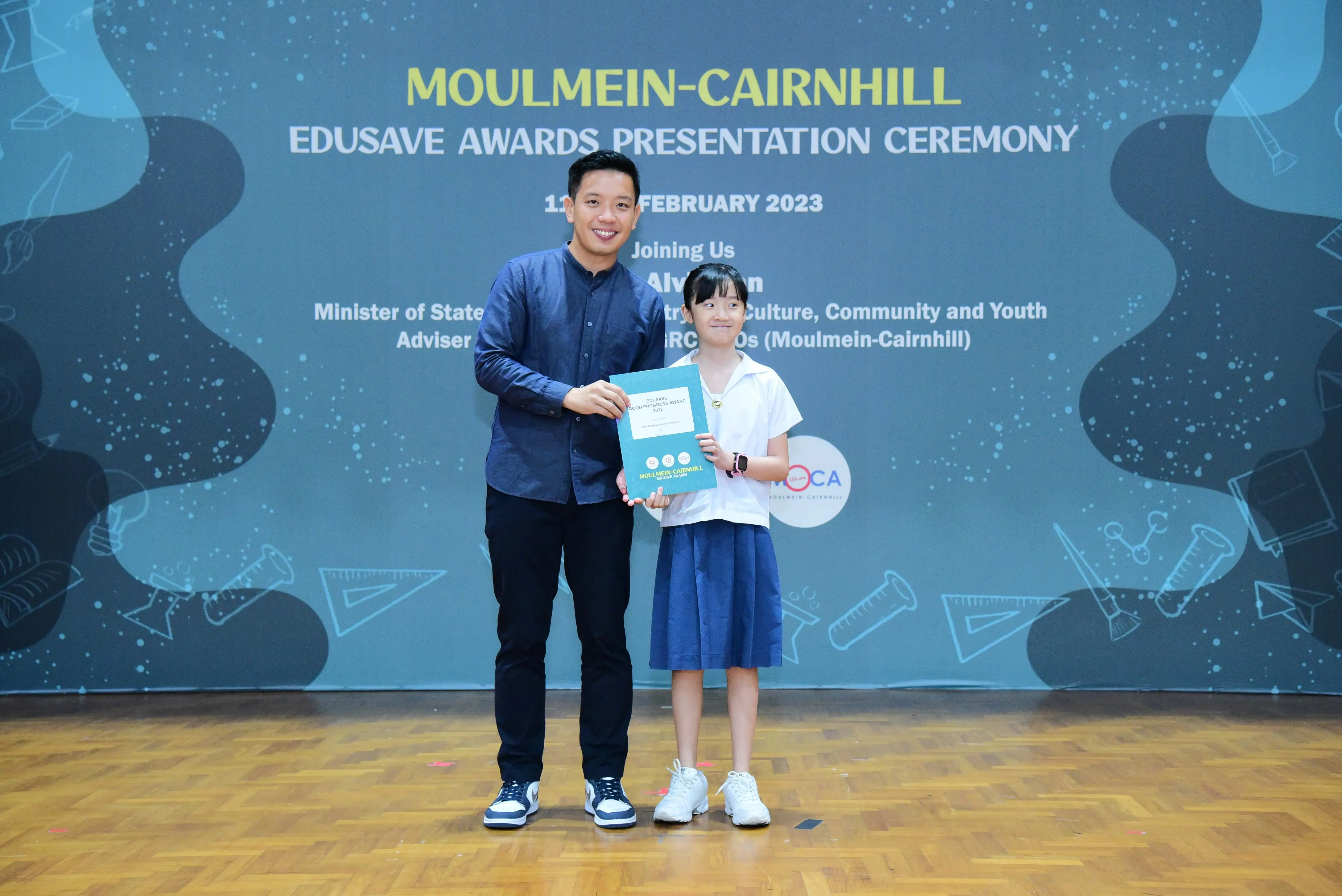 A man and a young girl hold a certificate together at the Moulmein-Cairnhill Edusave Awards Presentation Ceremony 2023.