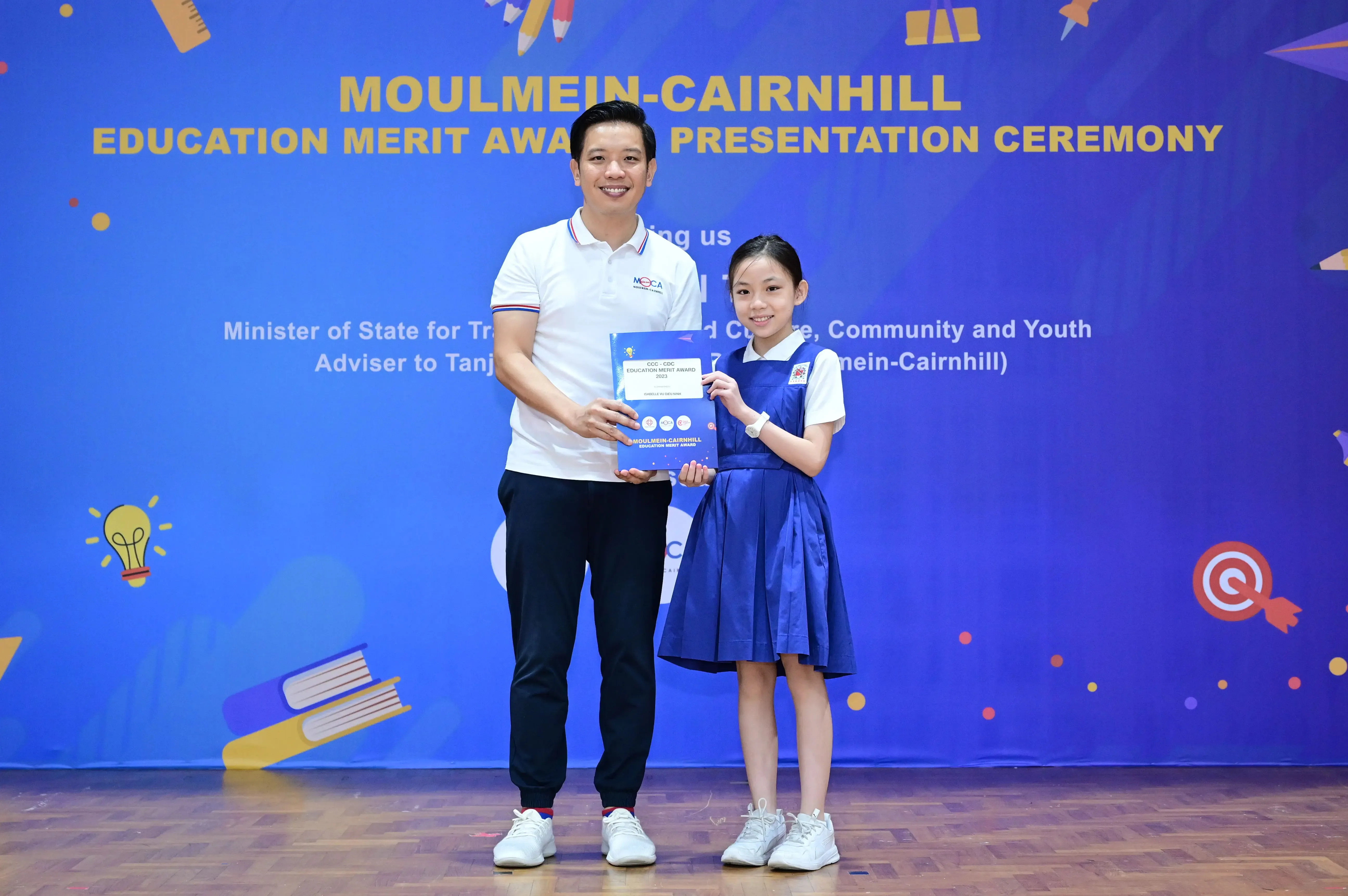 A man and a young girl hold an award certificate at the Moulmein-Cairnhill Education Merit Award Presentation Ceremony.