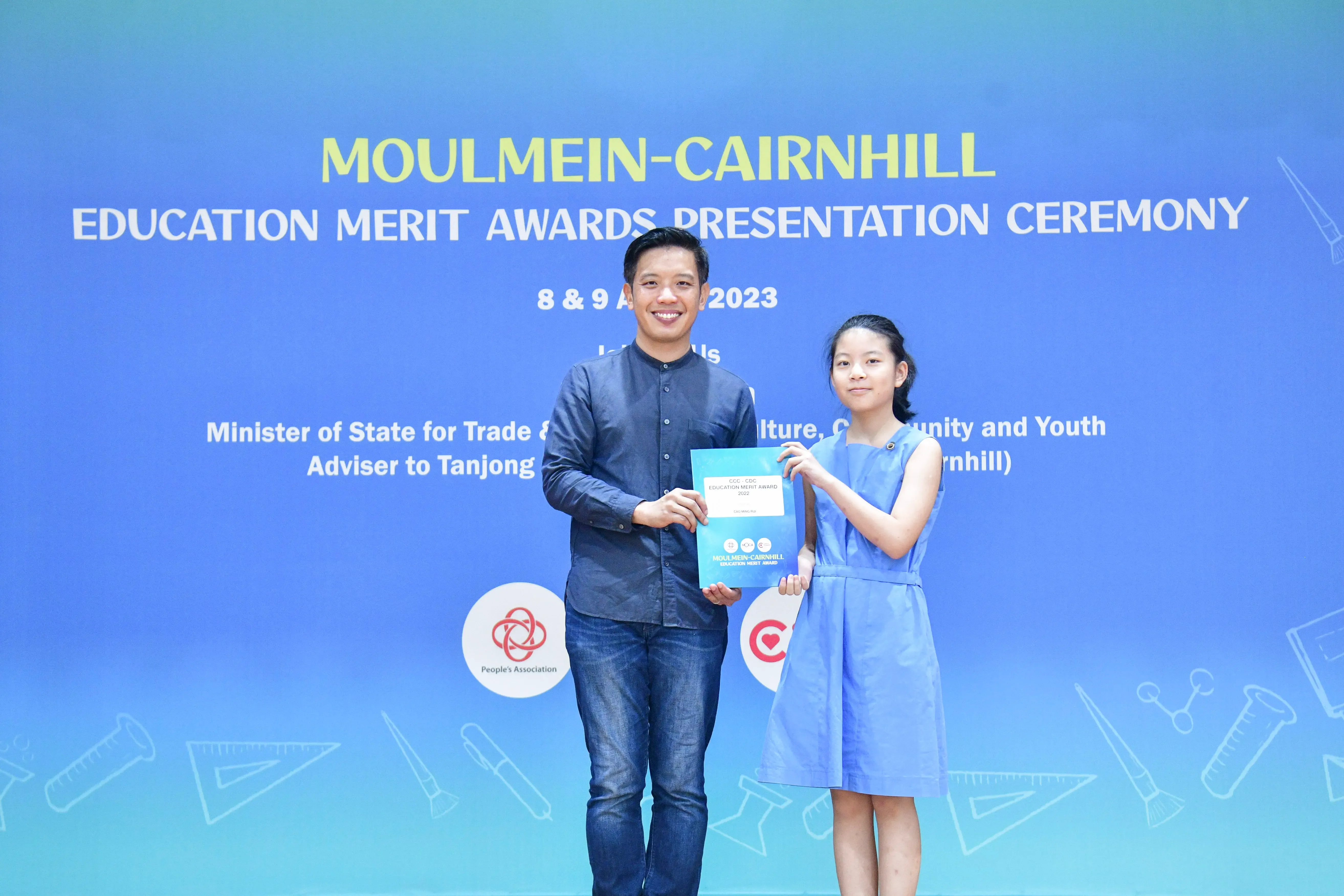 A man and a young girl hold a certificate together at the Moulmein-Cairnhill Education Merit Awards Ceremony 2023.