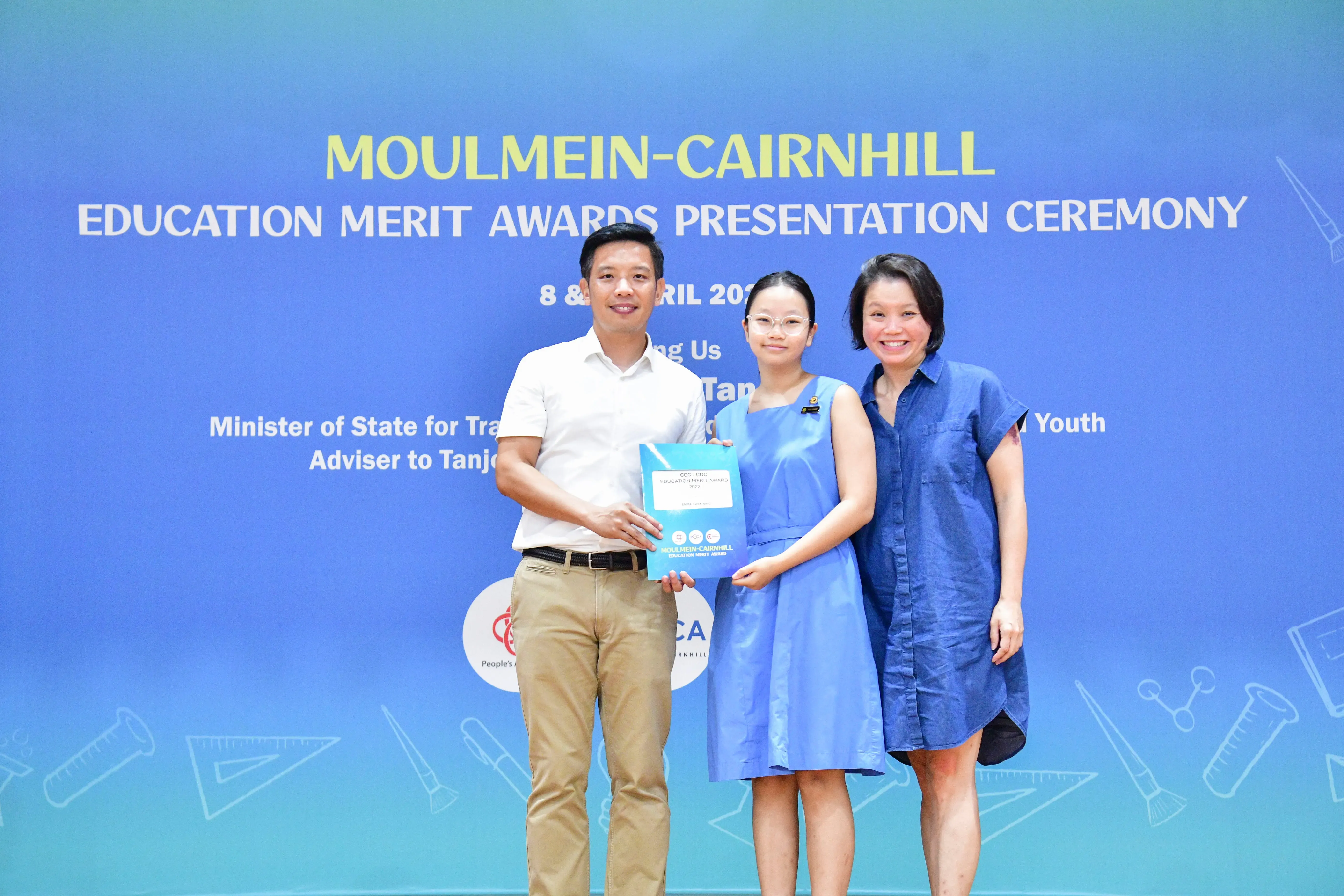 Three people pose at the Moulmein-Cairnhill Education Merit Awards Presentation Ceremony, with a girl holding an award folder.