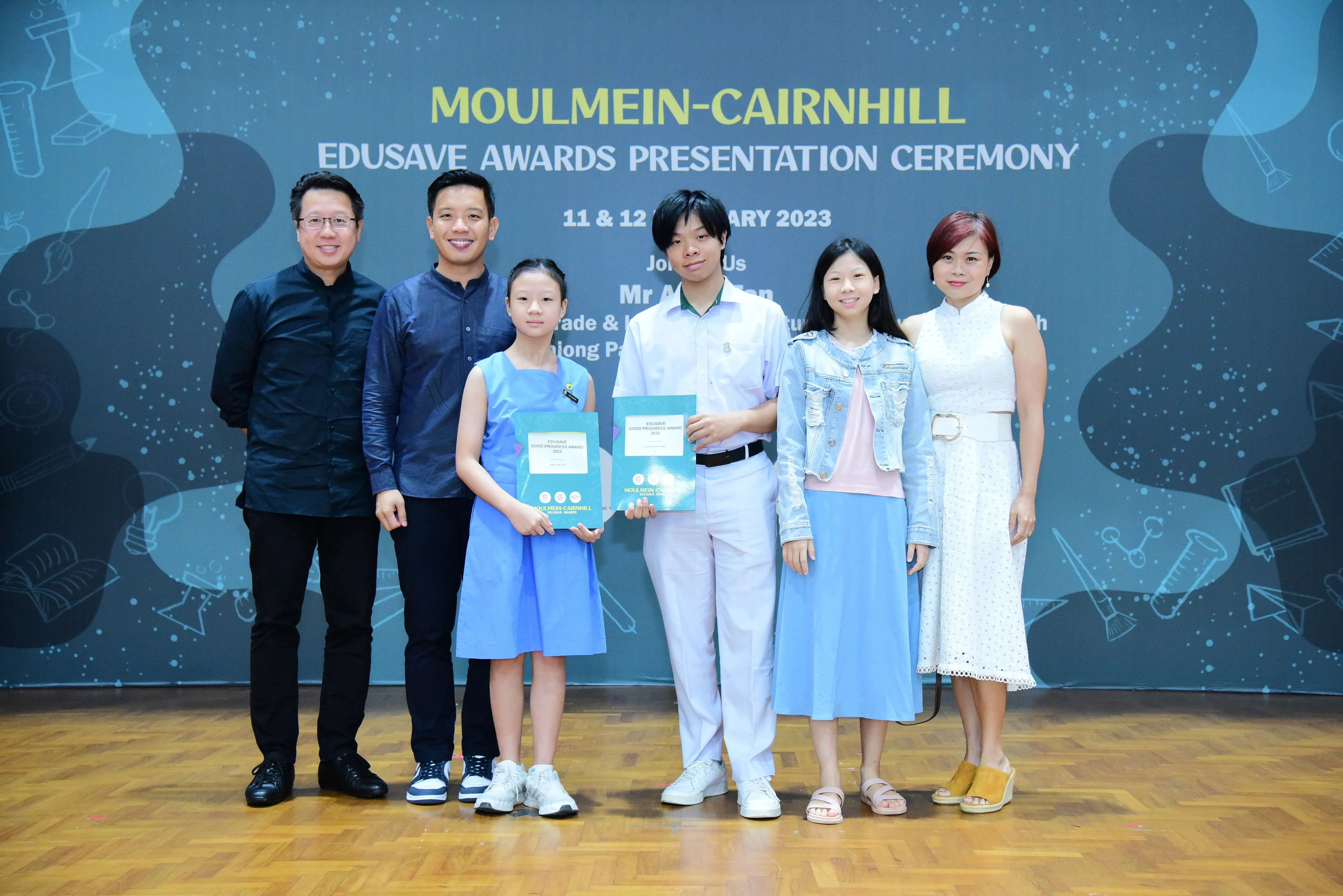 Six people pose at the Moulmein-Cairnhill Edusave Awards Presentation Ceremony 2023, two children holding award certificates.