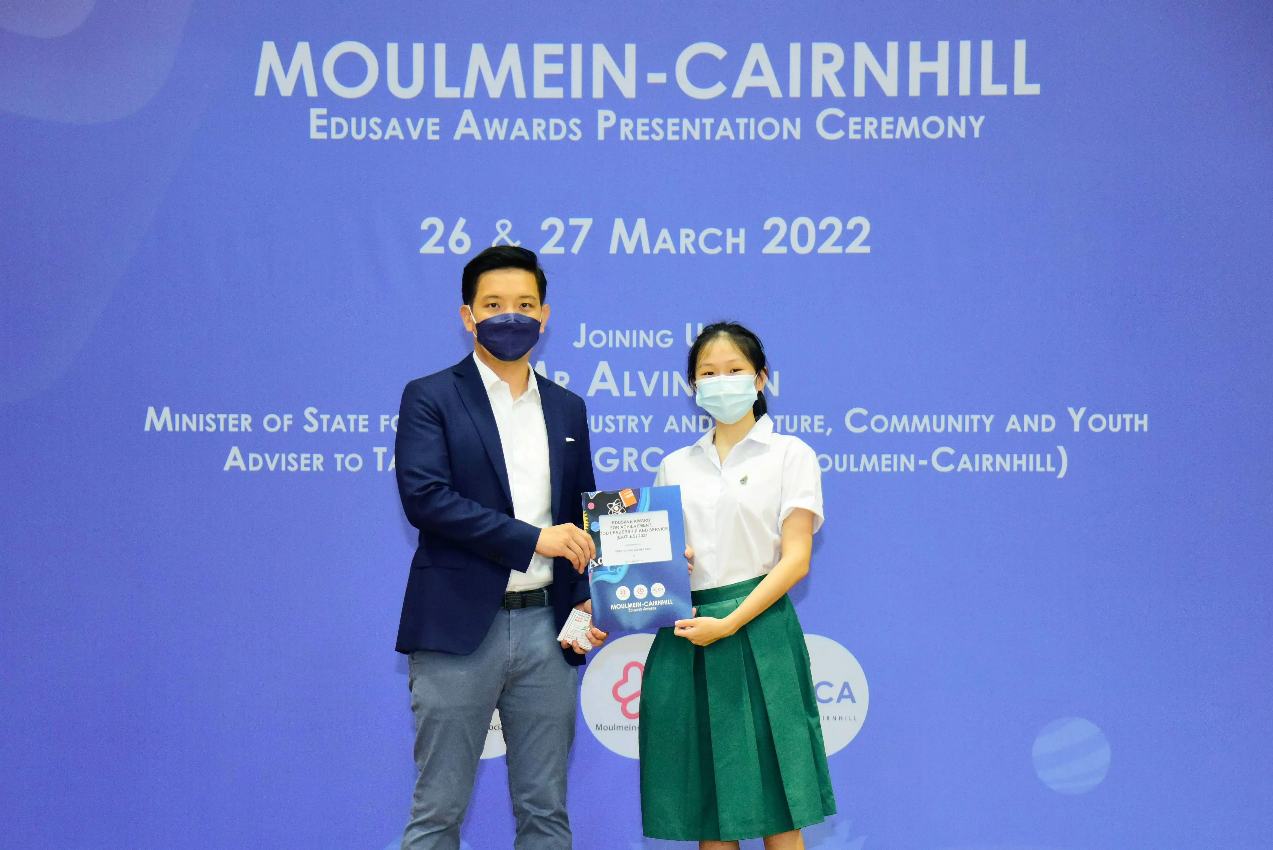 Two masked people hold an award booklet at the Moulmein-Cairnhill Edusave Awards Ceremony on March 26-27, 2022.