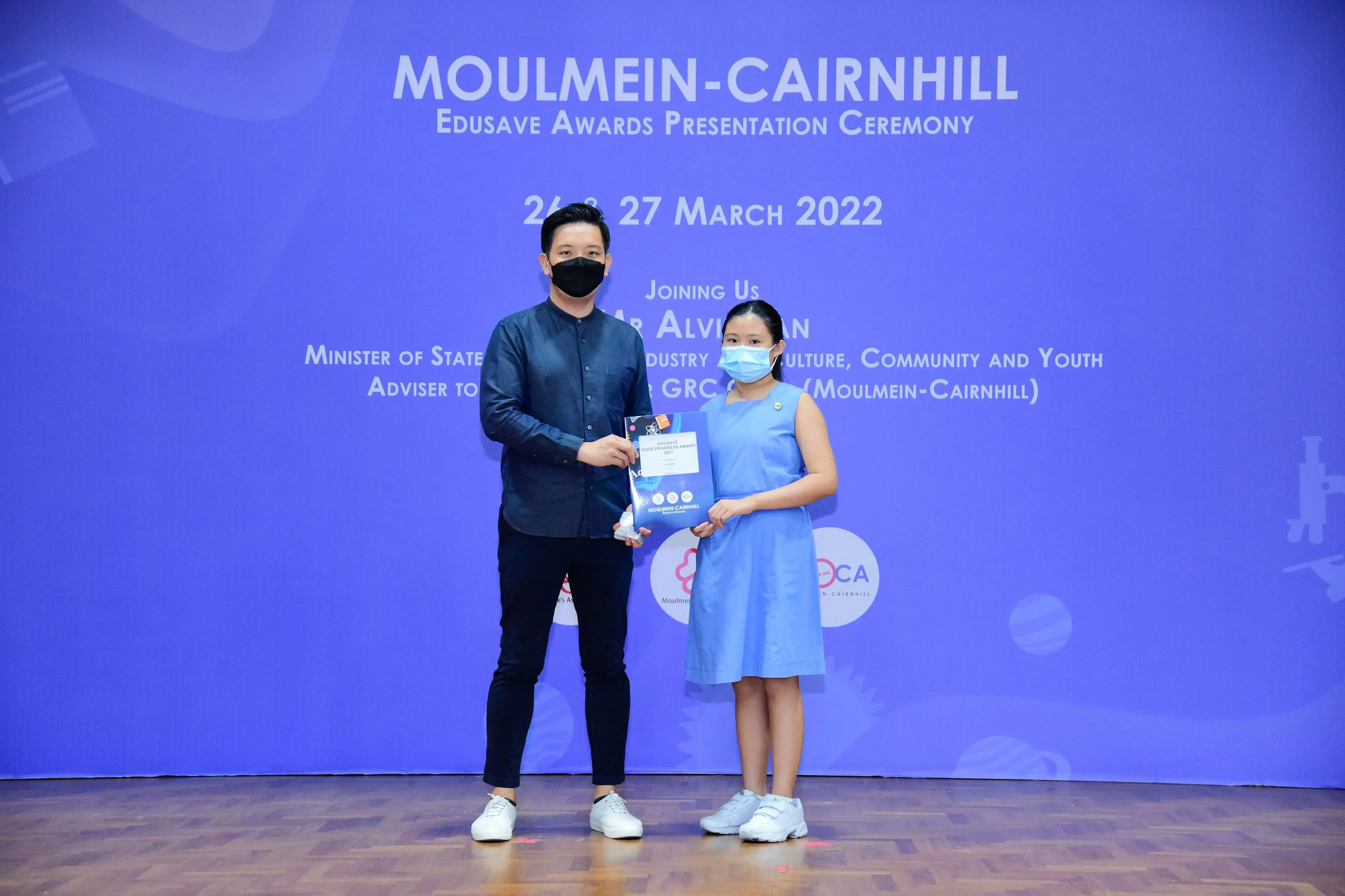 A masked man and a young girl hold an award certificate at the Moulmein-Cairnhill Edusave Awards Ceremony, March 2022.