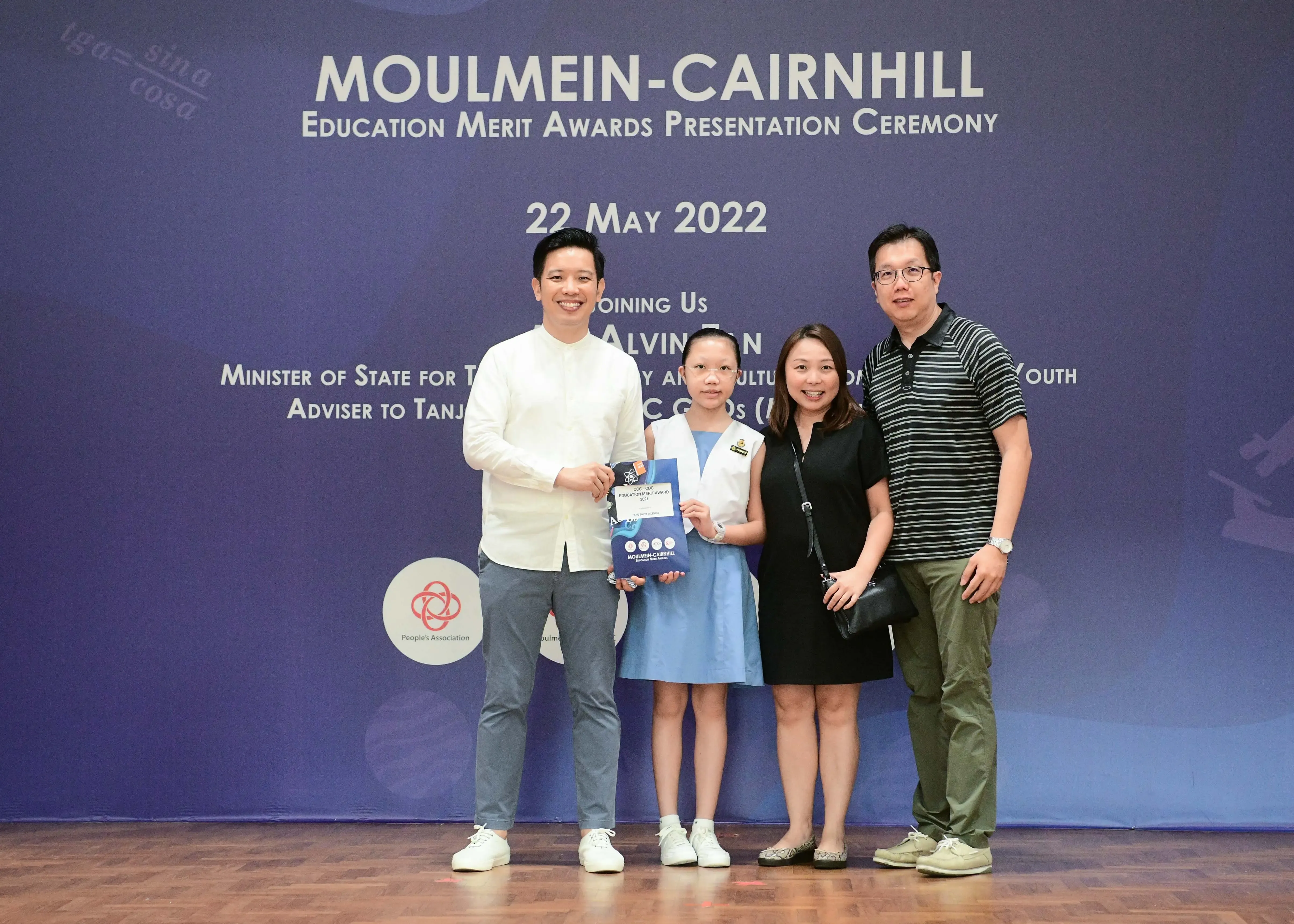 Four people pose at the Moulmein-Cairnhill Education Merit Awards ceremony on 22 May 2022, child holding an award folder.