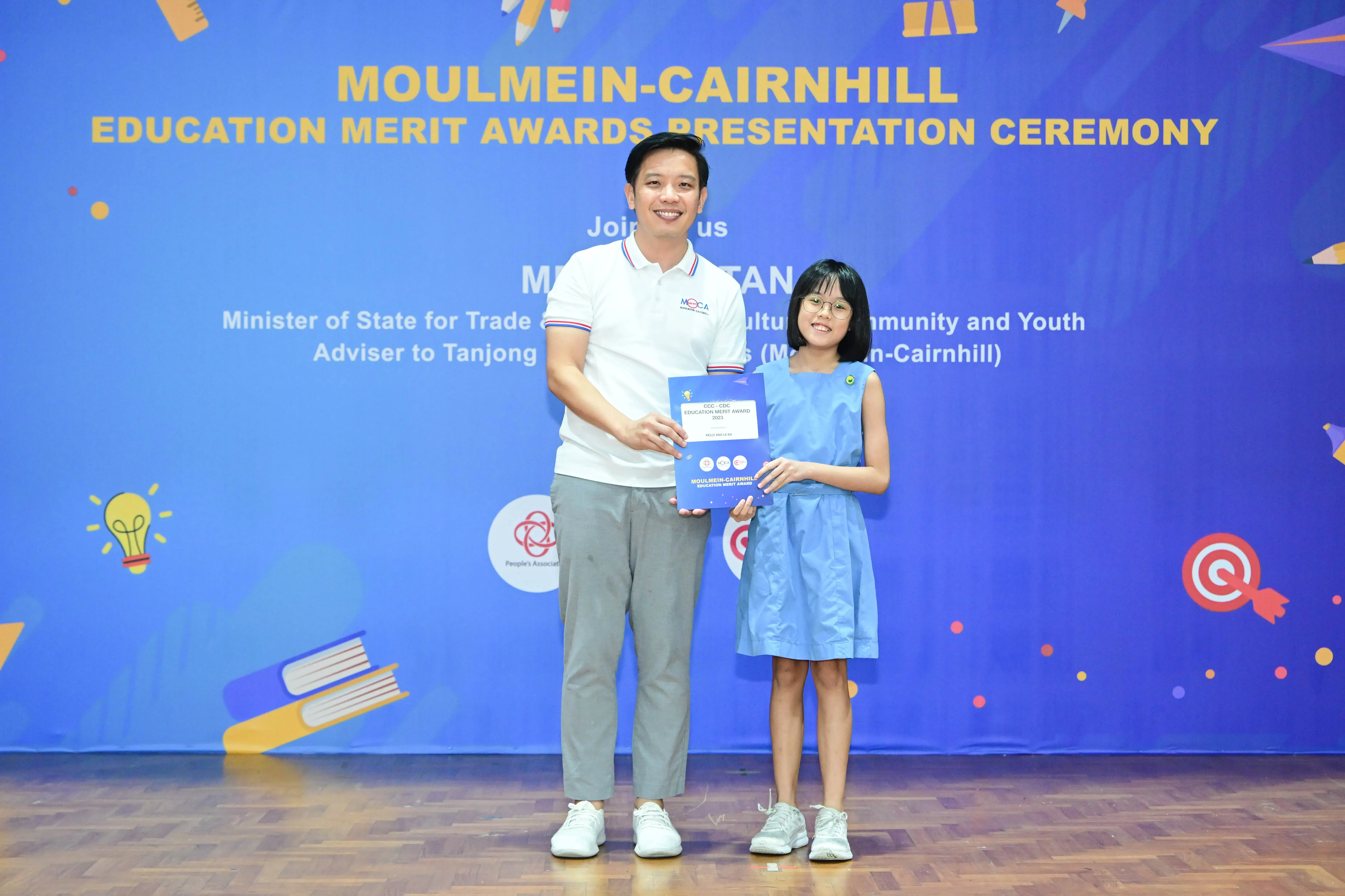 A man and a young girl hold a certificate together at the Moulmein-Cairnhill Education Merit Awards Presentation Ceremony.