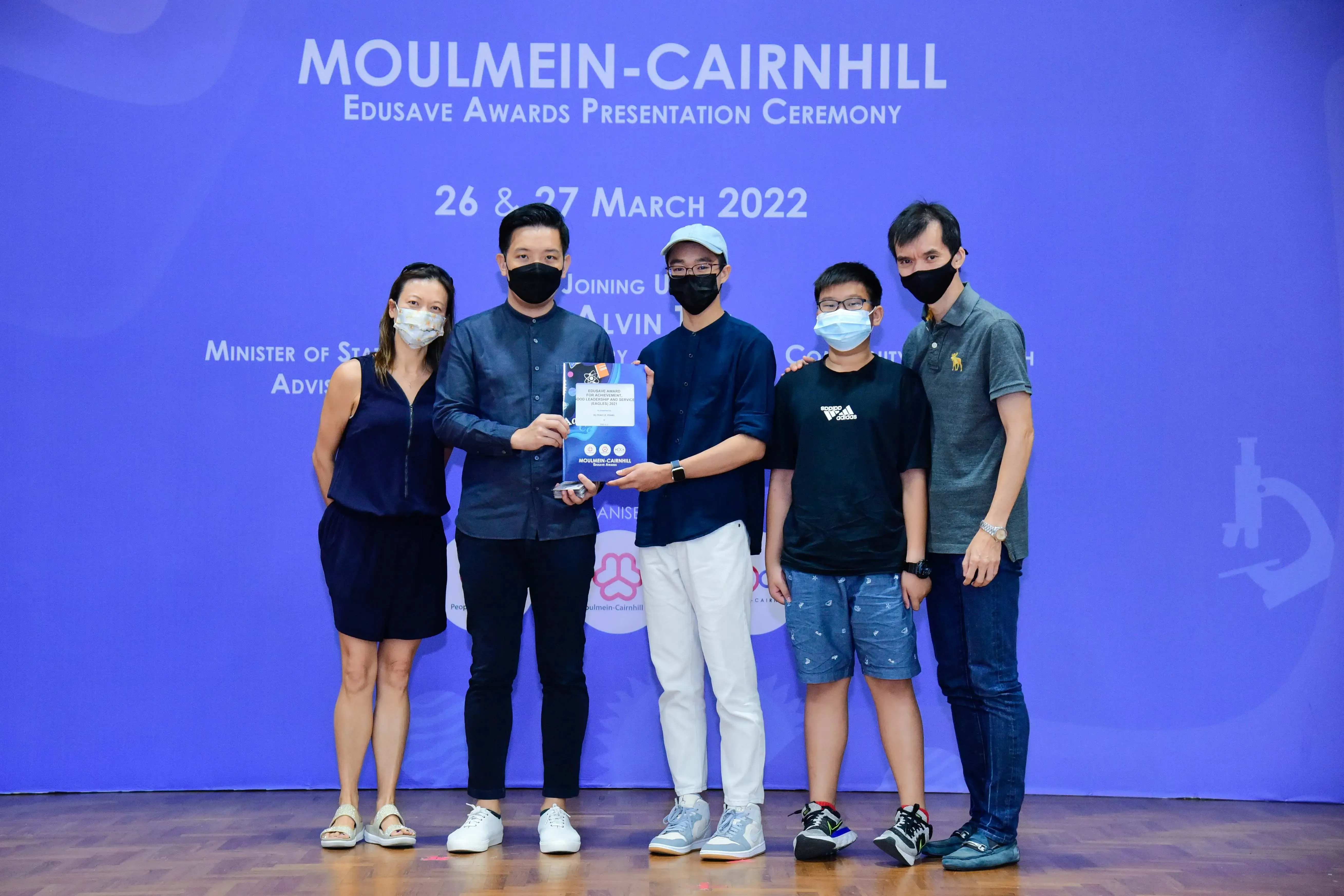 Five masked people pose on stage at the Moulmein-Cairnhill Edusave Awards Presentation Ceremony, March 2022.