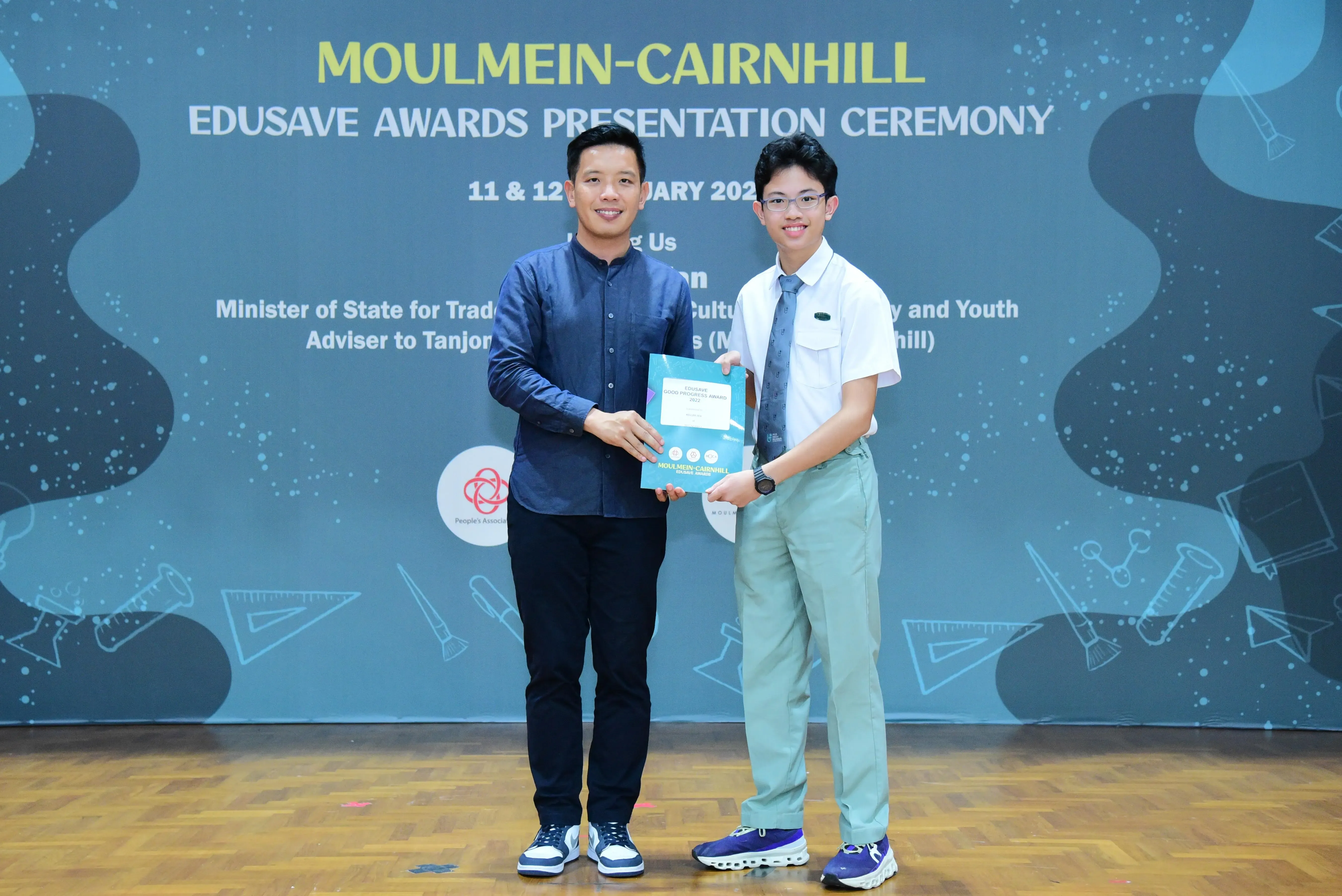 Two people smile while holding a certificate at the Moulmein-Cairnhill Edusave Awards Presentation Ceremony.