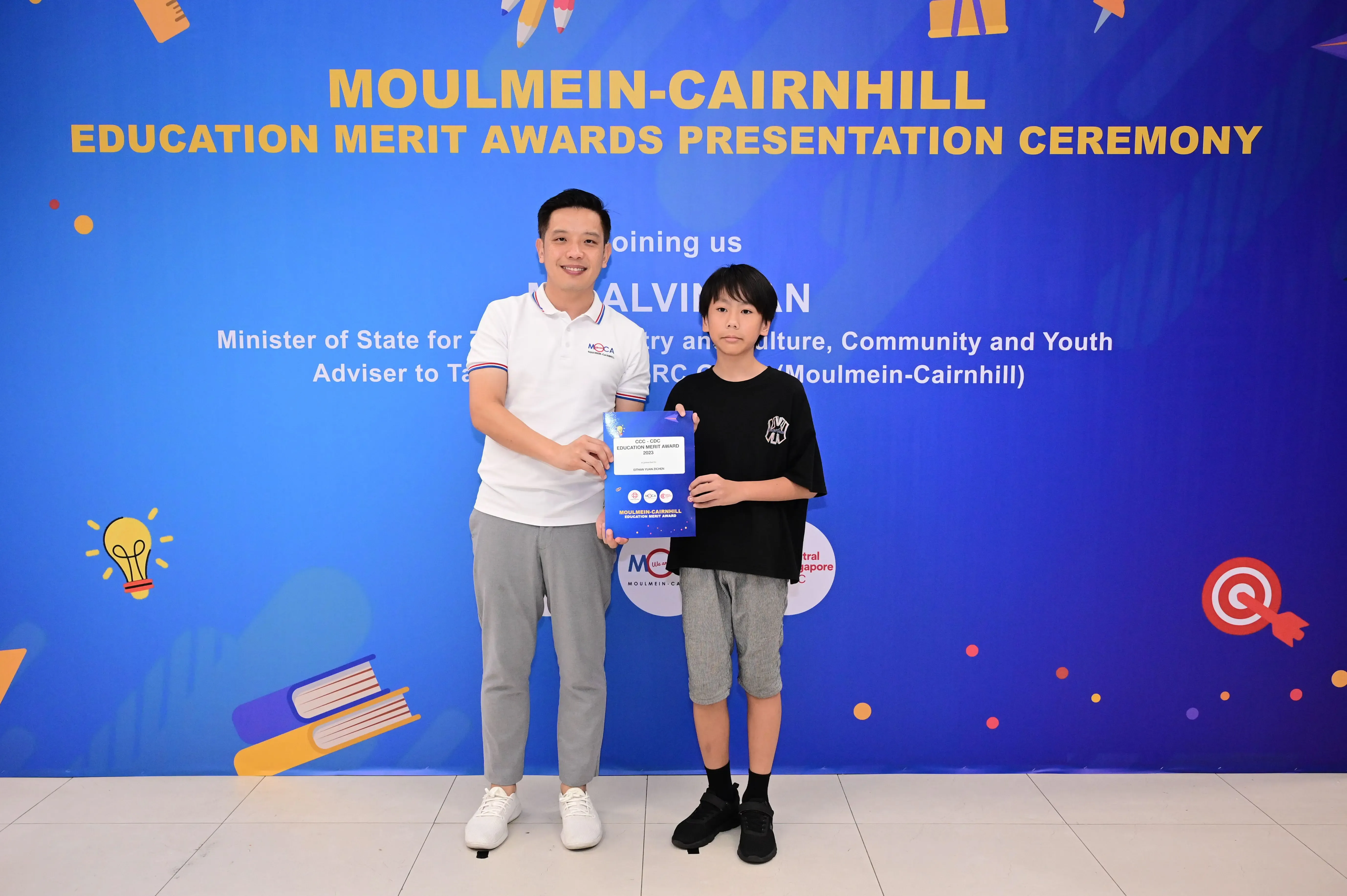 A man and a young boy hold an award certificate at the Moulmein-Cairnhill Education Merit Awards Presentation Ceremony.