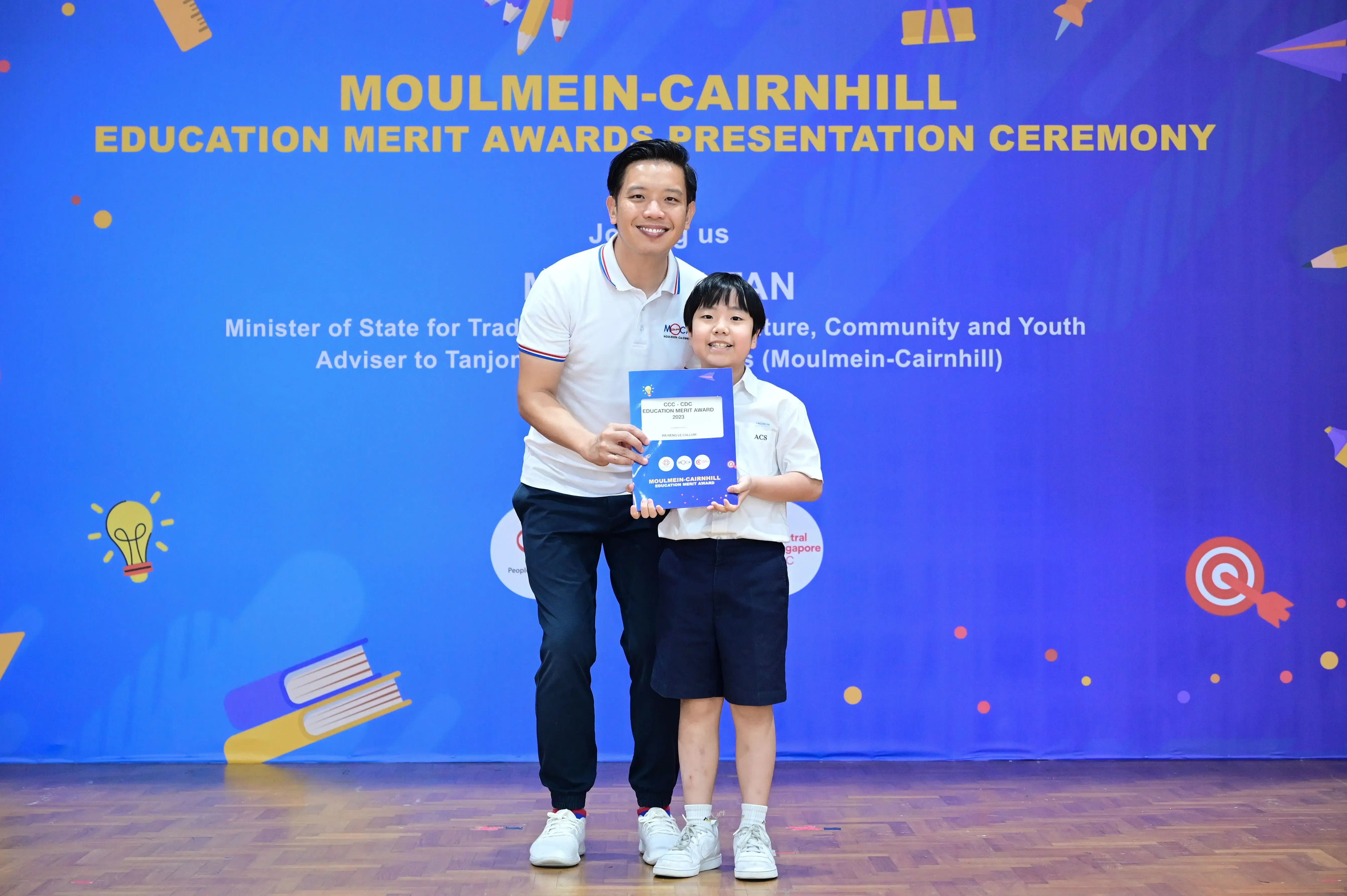 A man and a young boy hold a certificate together at the Moulmein-Cairnhill Education Merit Awards ceremony.