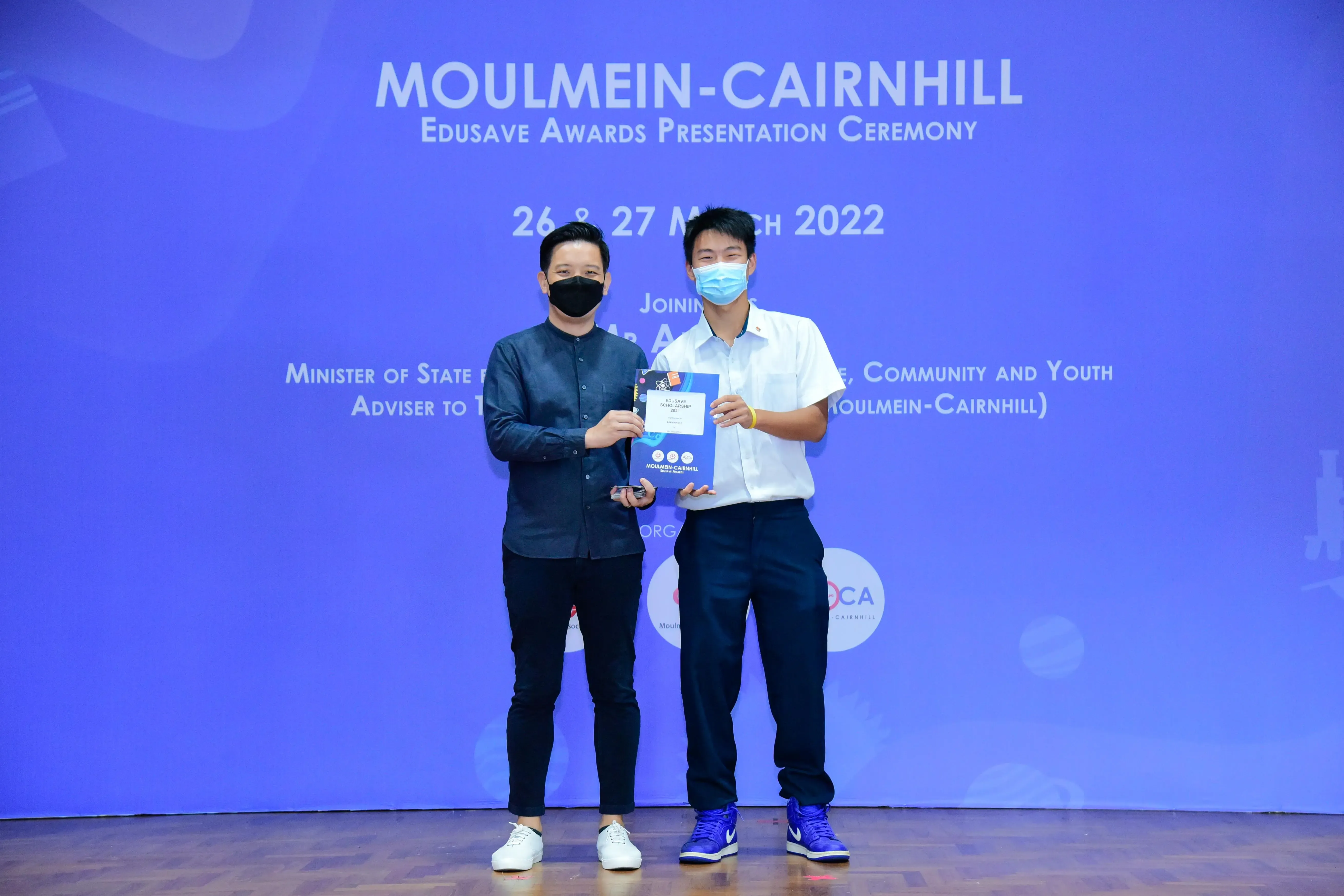 Two masked men hold an award certificate at the Moulmein-Cairnhill Edusave Awards Ceremony, March 2022.