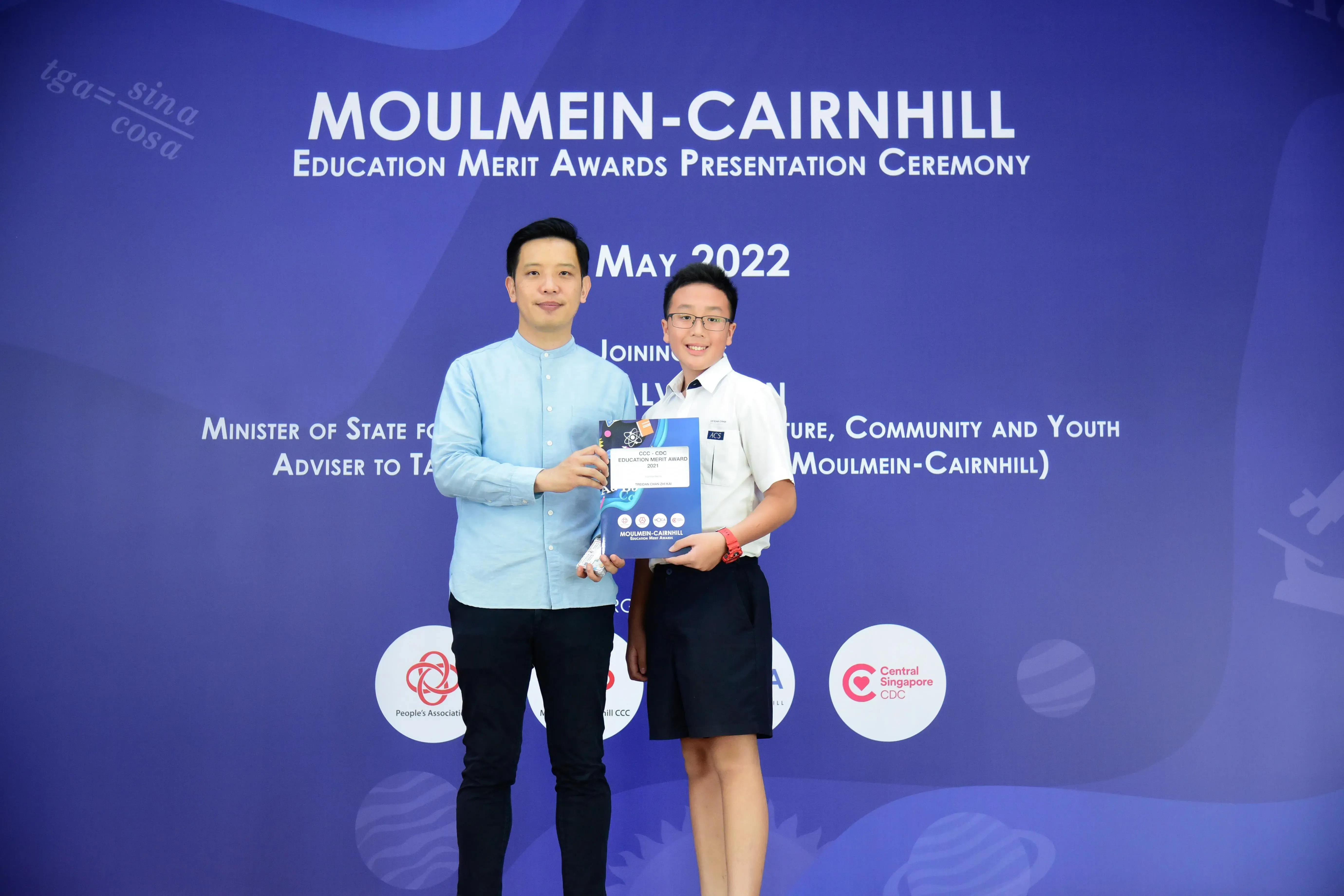 Two people pose holding an award booklet at the Moulmein-Cairnhill Education Merit Awards Ceremony, May 2022.