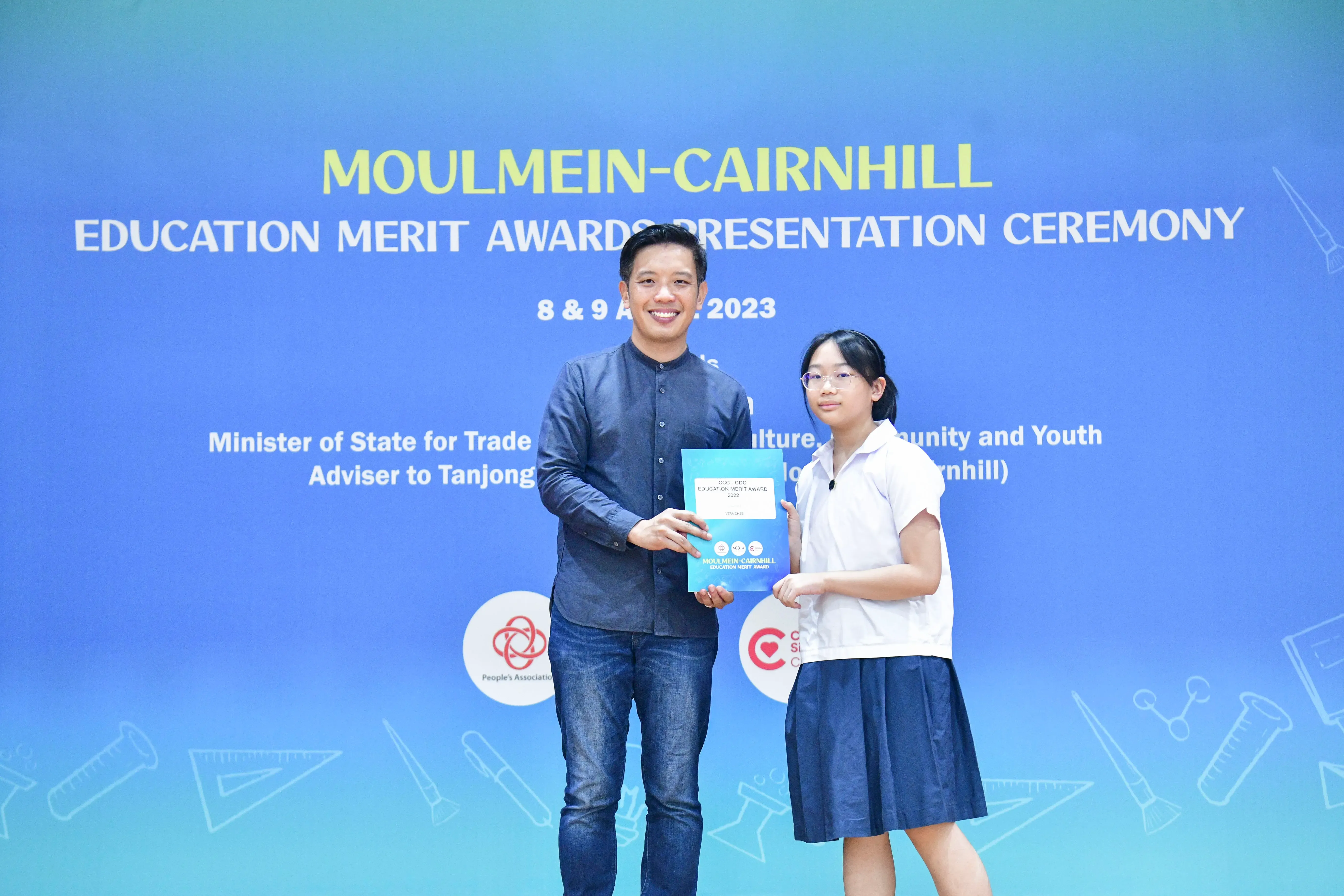 A man and a young girl in school uniform hold a certificate together at the Moulmein-Cairnhill Education Merit Awards 2023.