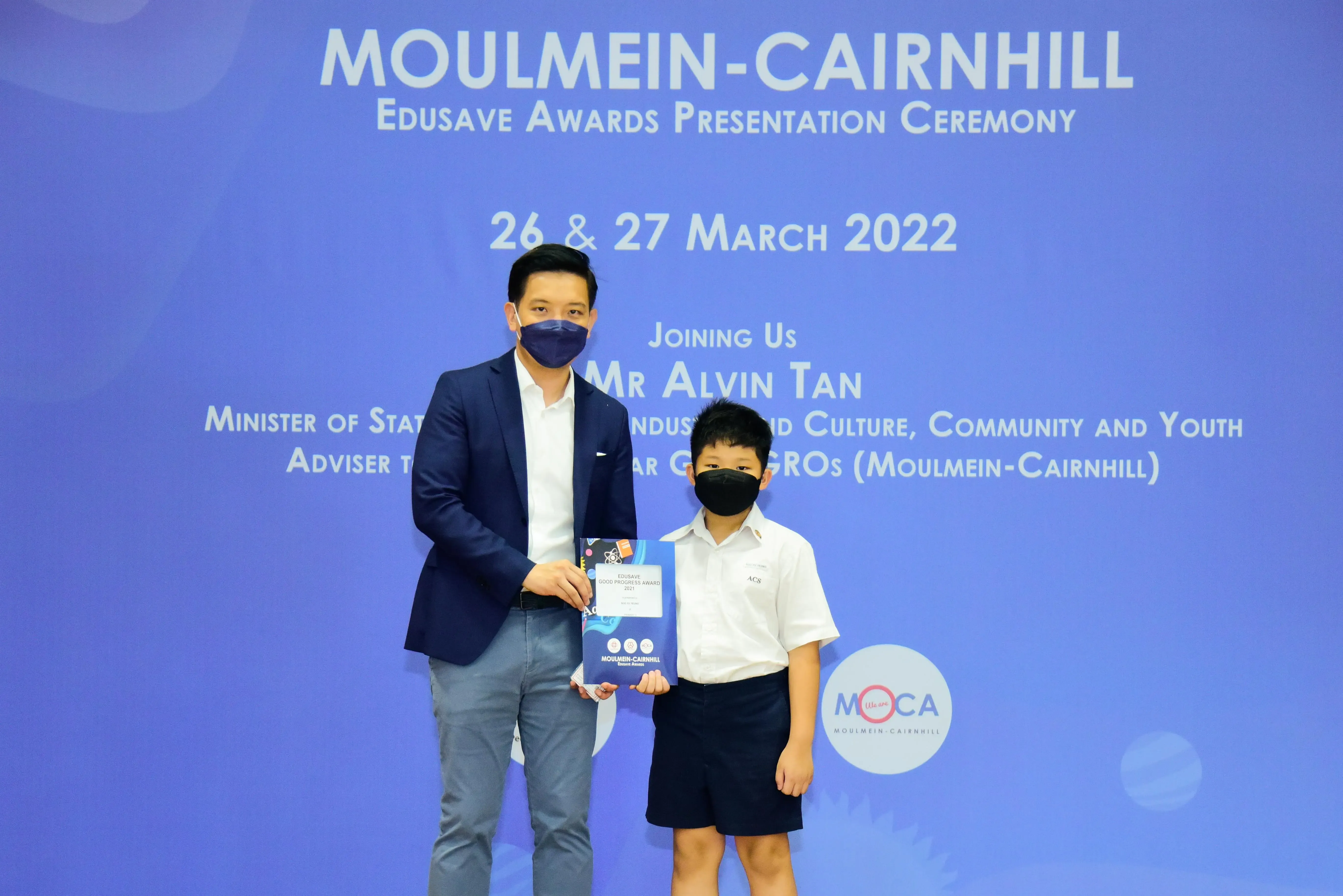 An adult and a young student in school uniform hold an award certificate at the Moulmein-Cairnhill Edusave Awards Ceremony 2022.