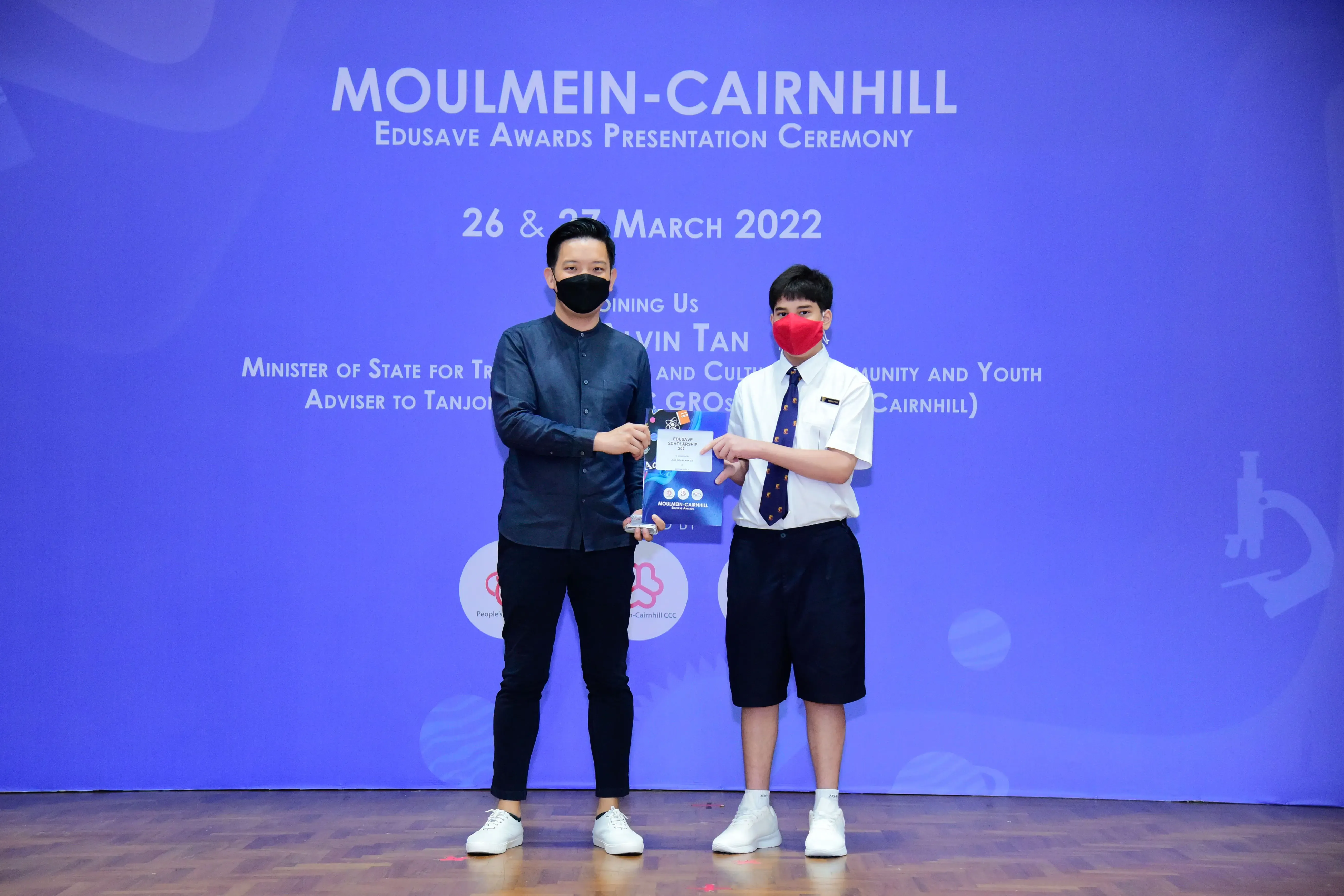 Two masked individuals hold an award at the Moulmein-Cairnhill Edusave Awards Presentation Ceremony, March 2022.