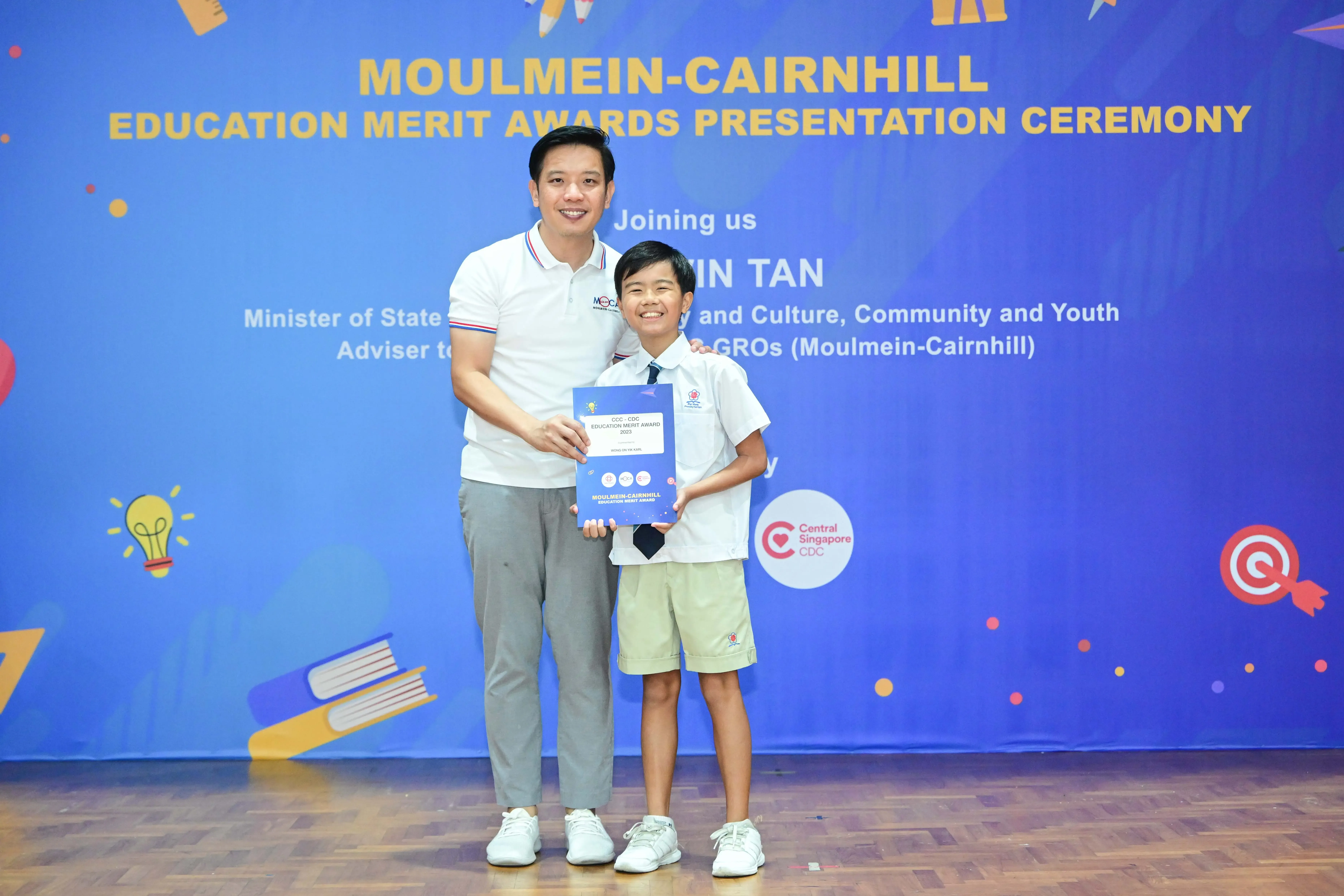 A man and a young boy hold an award certificate at the Moulmein-Cairnhill Education Merit Awards Presentation Ceremony.