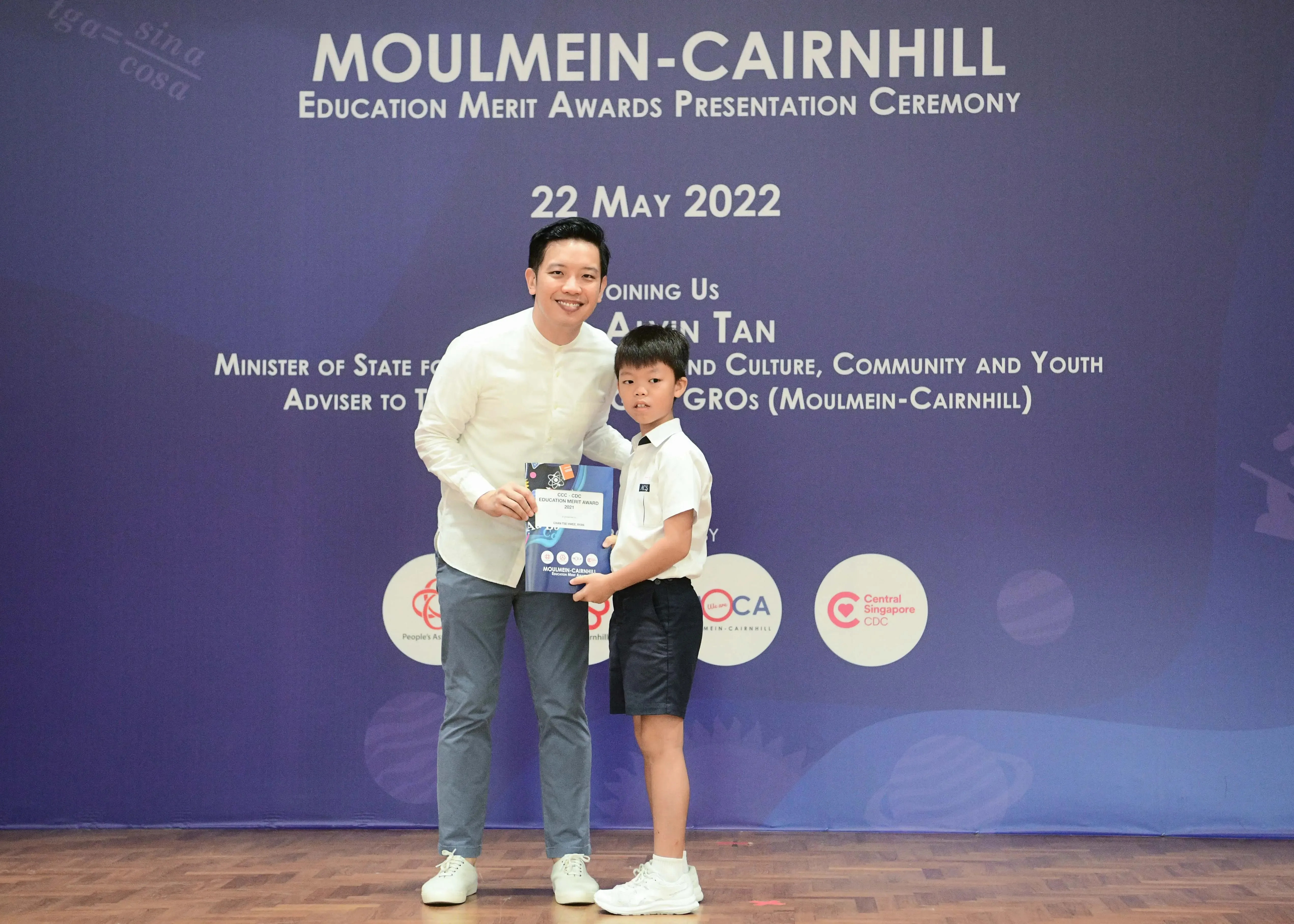 Man and young boy hold an award certificate at Moulmein-Cairnhill Education Merit Awards Ceremony, 22 May 2022.