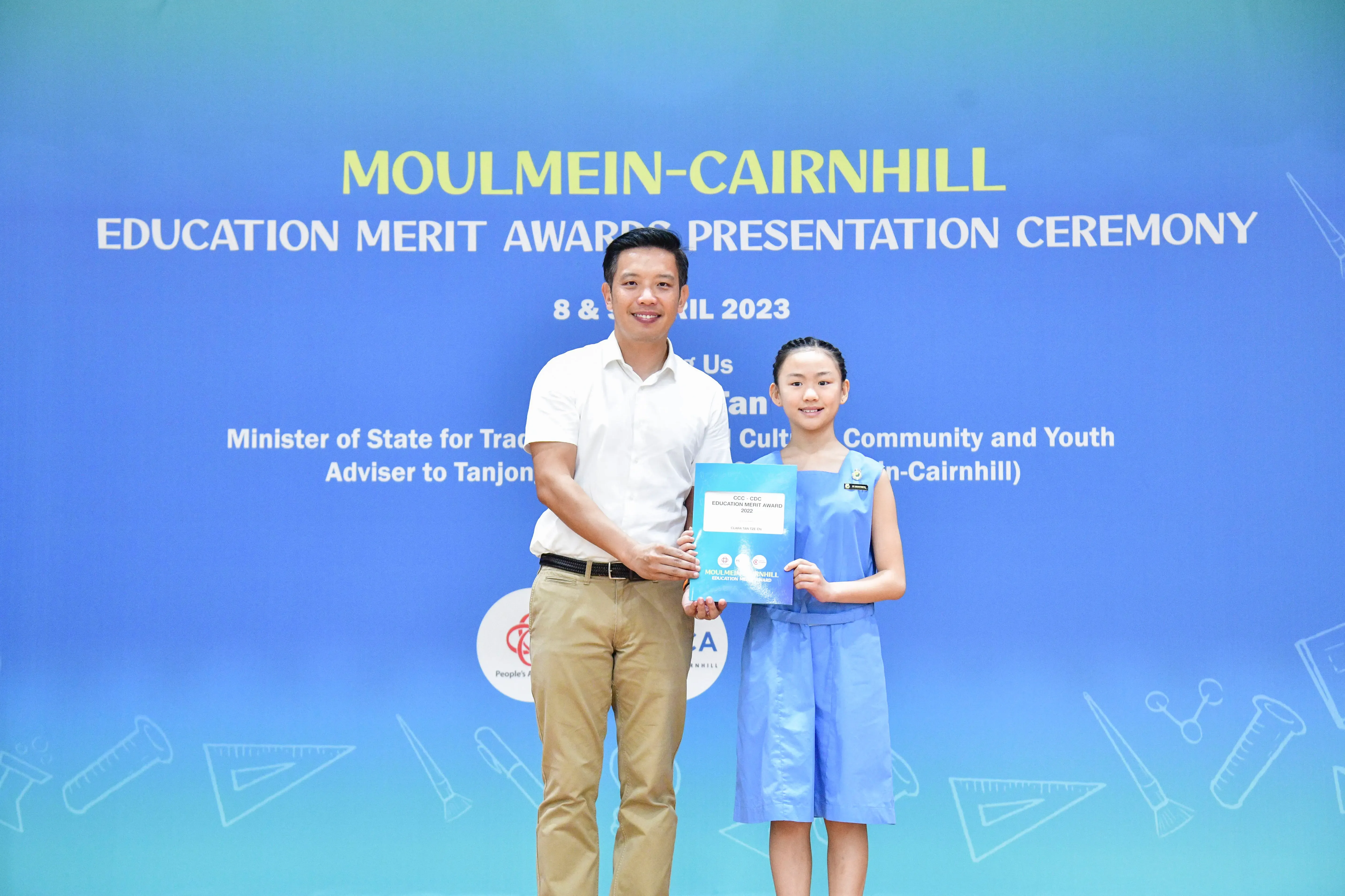 A man and a young girl hold a certificate together at the Moulmein-Cairnhill Education Merit Awards Ceremony 2023.