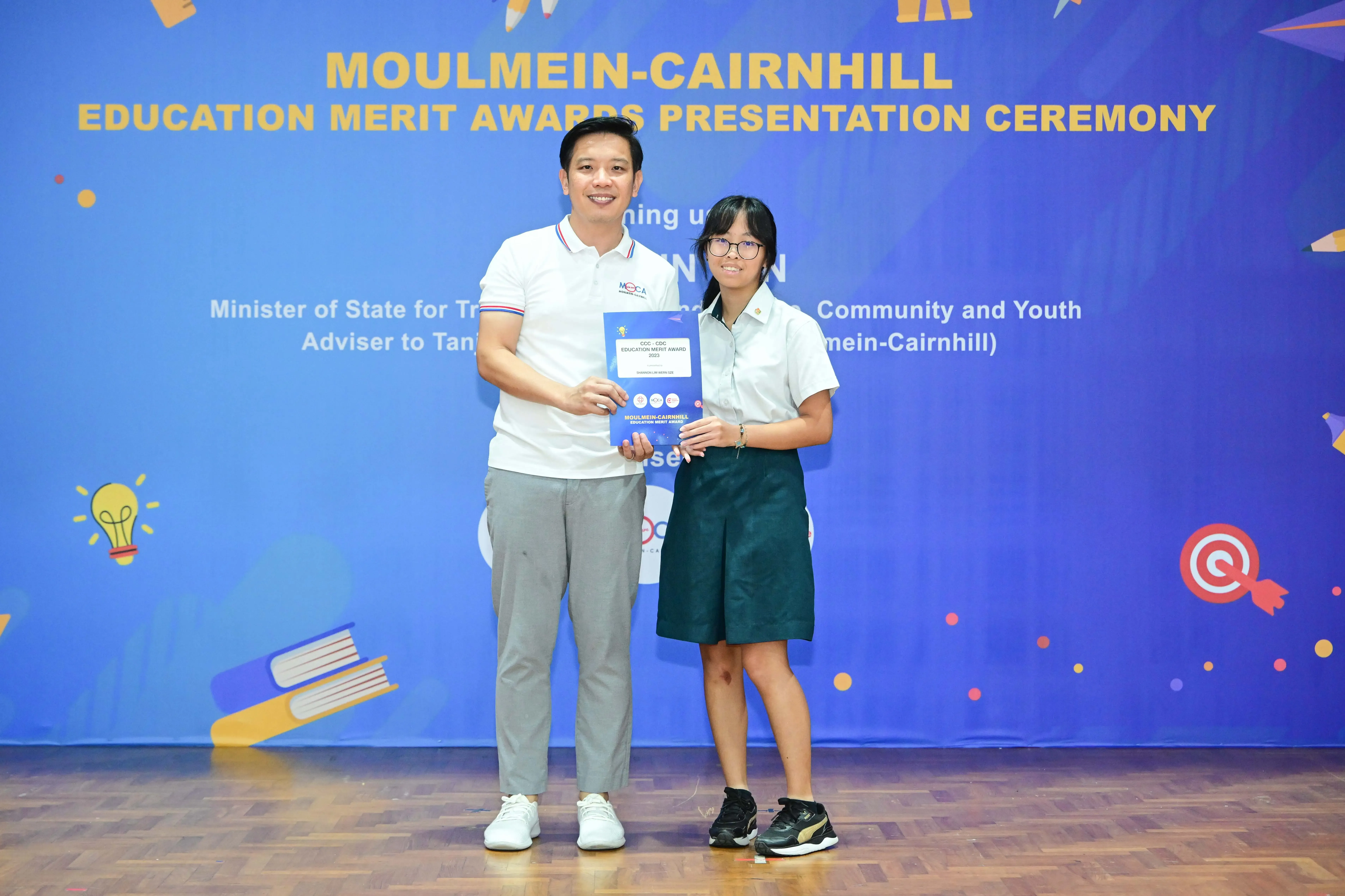 A man and a young girl in school uniform hold a certificate at the Moulmein-Cairnhill Education Merit Awards ceremony.