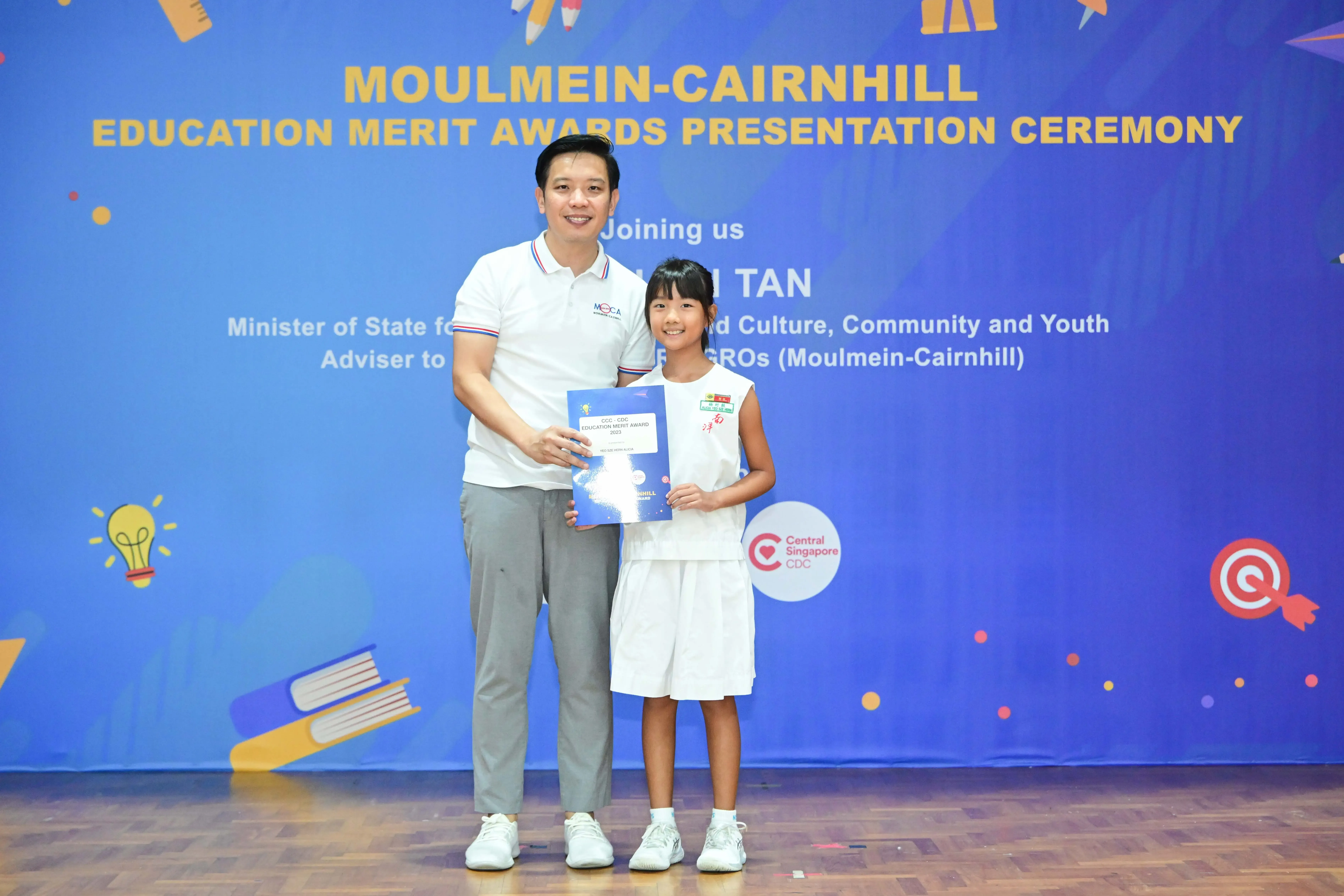 A man and a young girl hold a certificate together at the Moulmein-Cairnhill Education Merit Awards Presentation Ceremony.