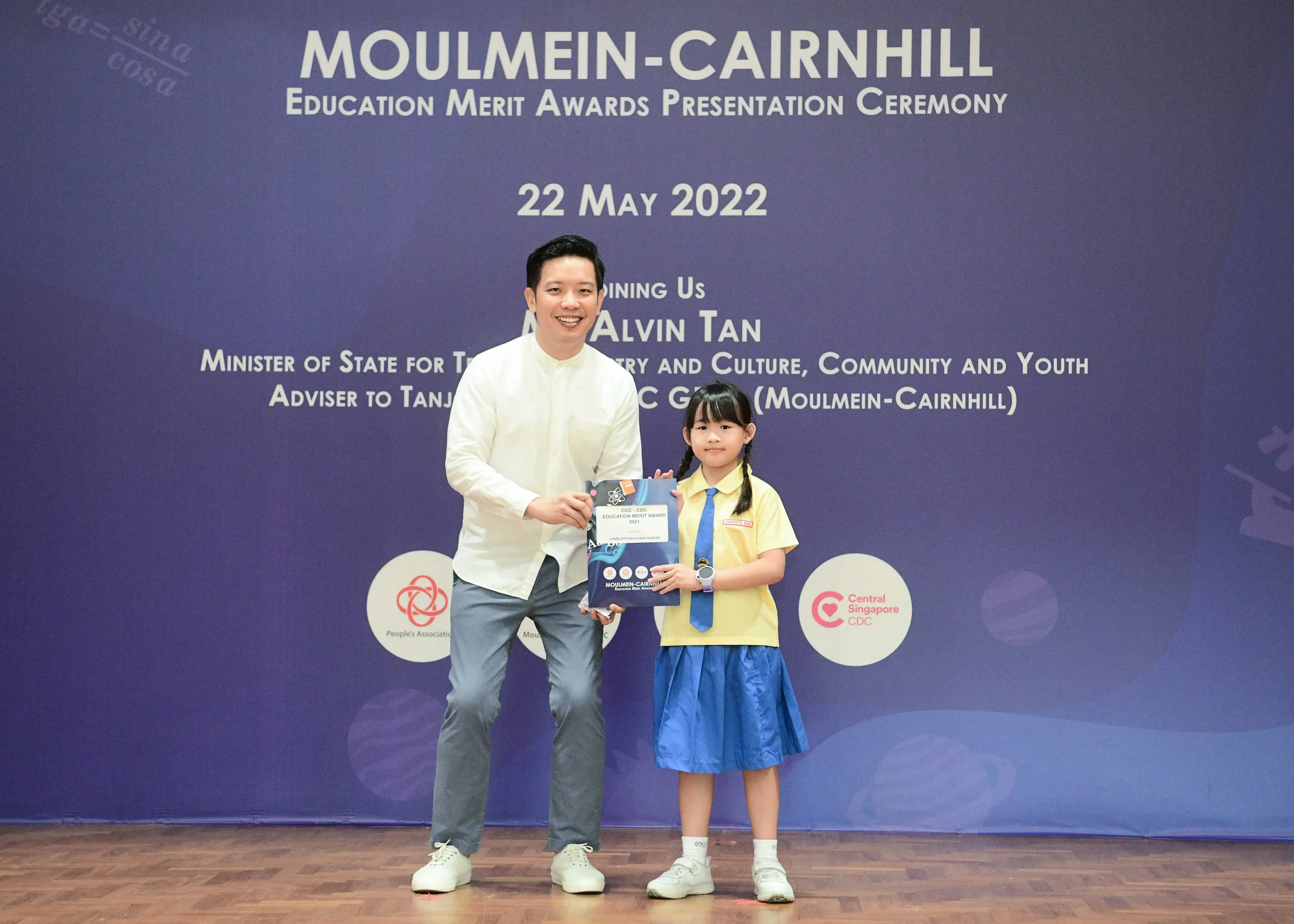 A man and a young girl in school uniform hold an award certificate at the Moulmein-Cairnhill Education Merit Awards 2022.