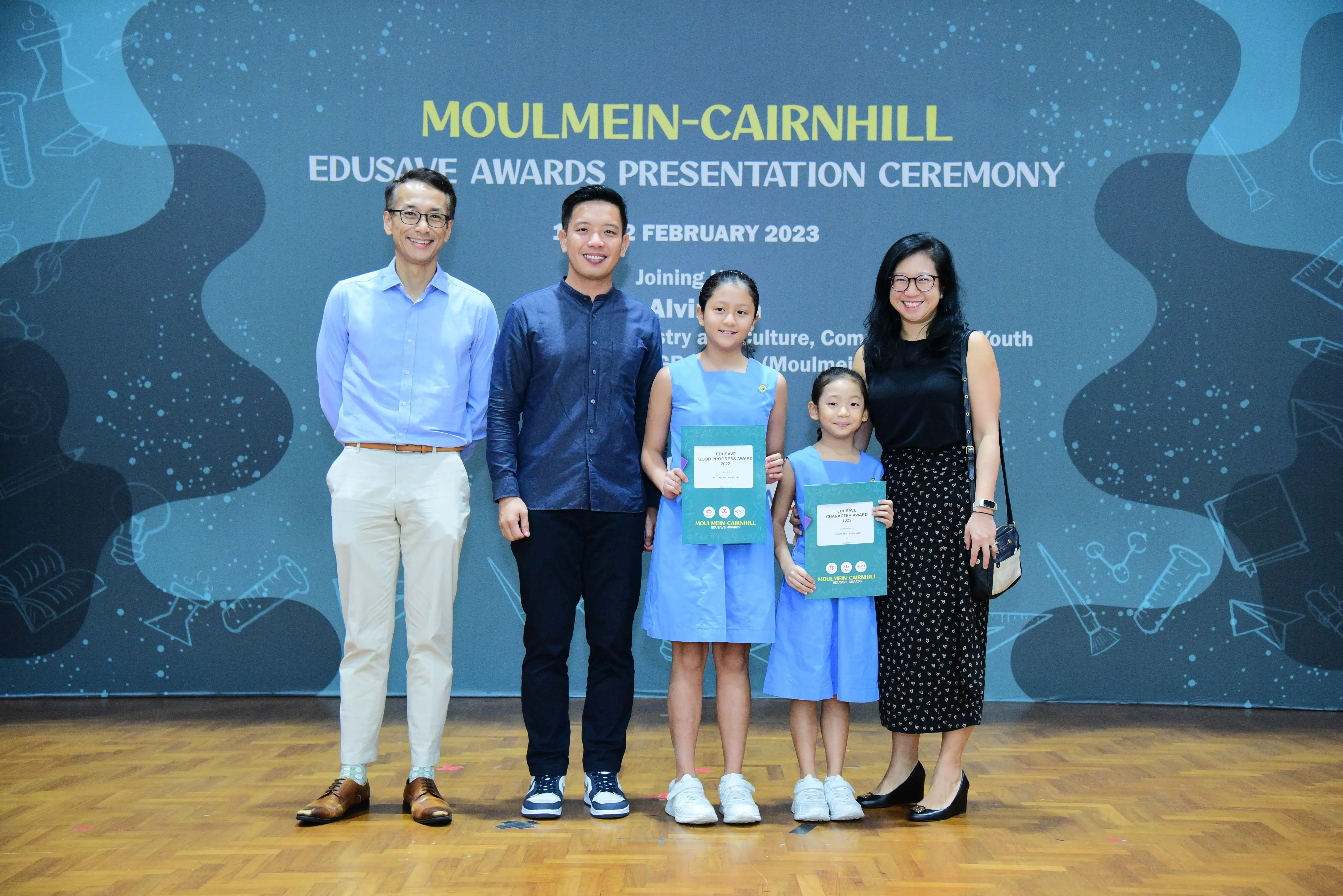 Five people pose at the Moulmein-Cairnhill Edusave Awards Presentation Ceremony, two girls holding award certificates.