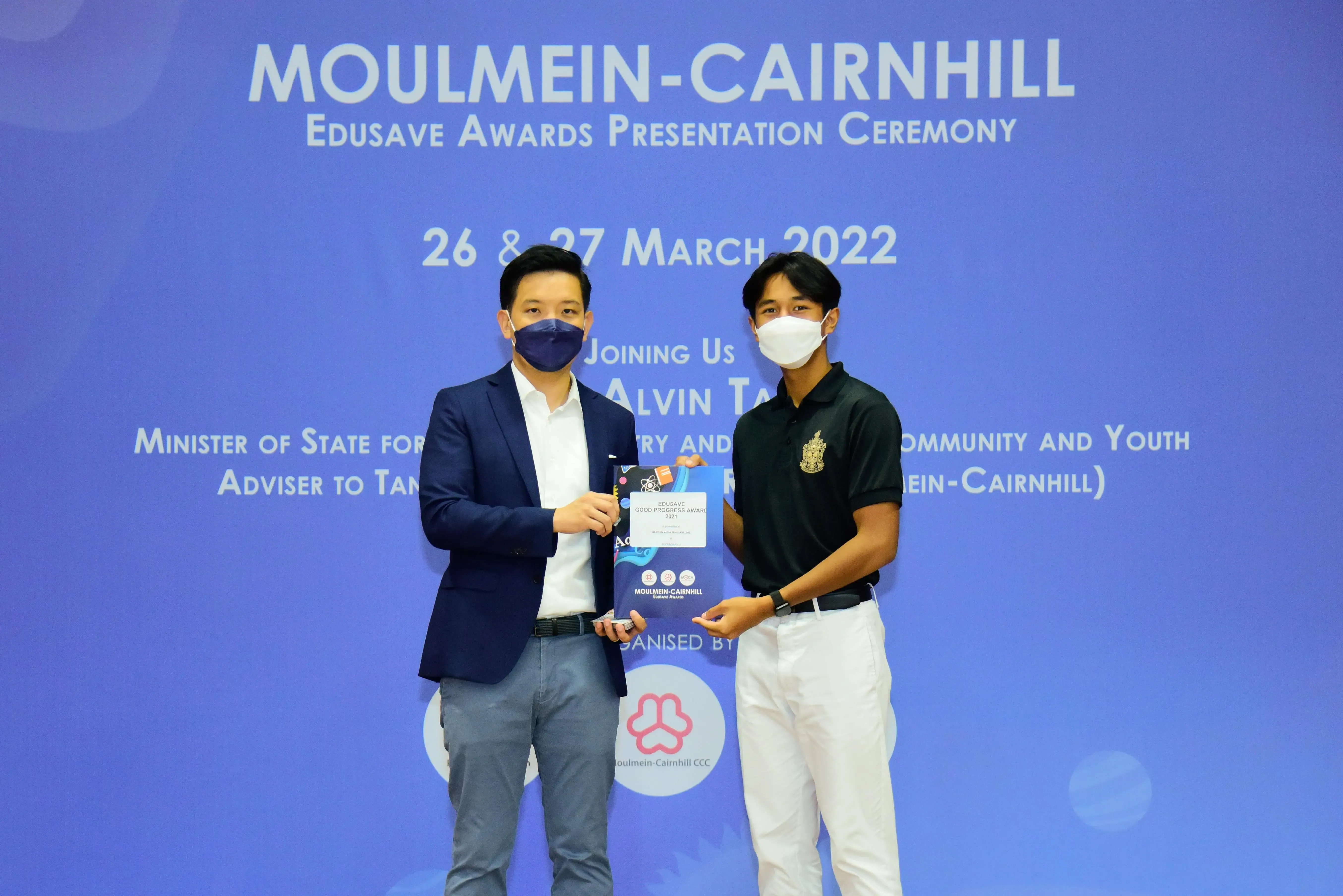 Two masked men hold an award certificate at the Moulmein-Cairnhill Edusave Awards Ceremony, March 2022.