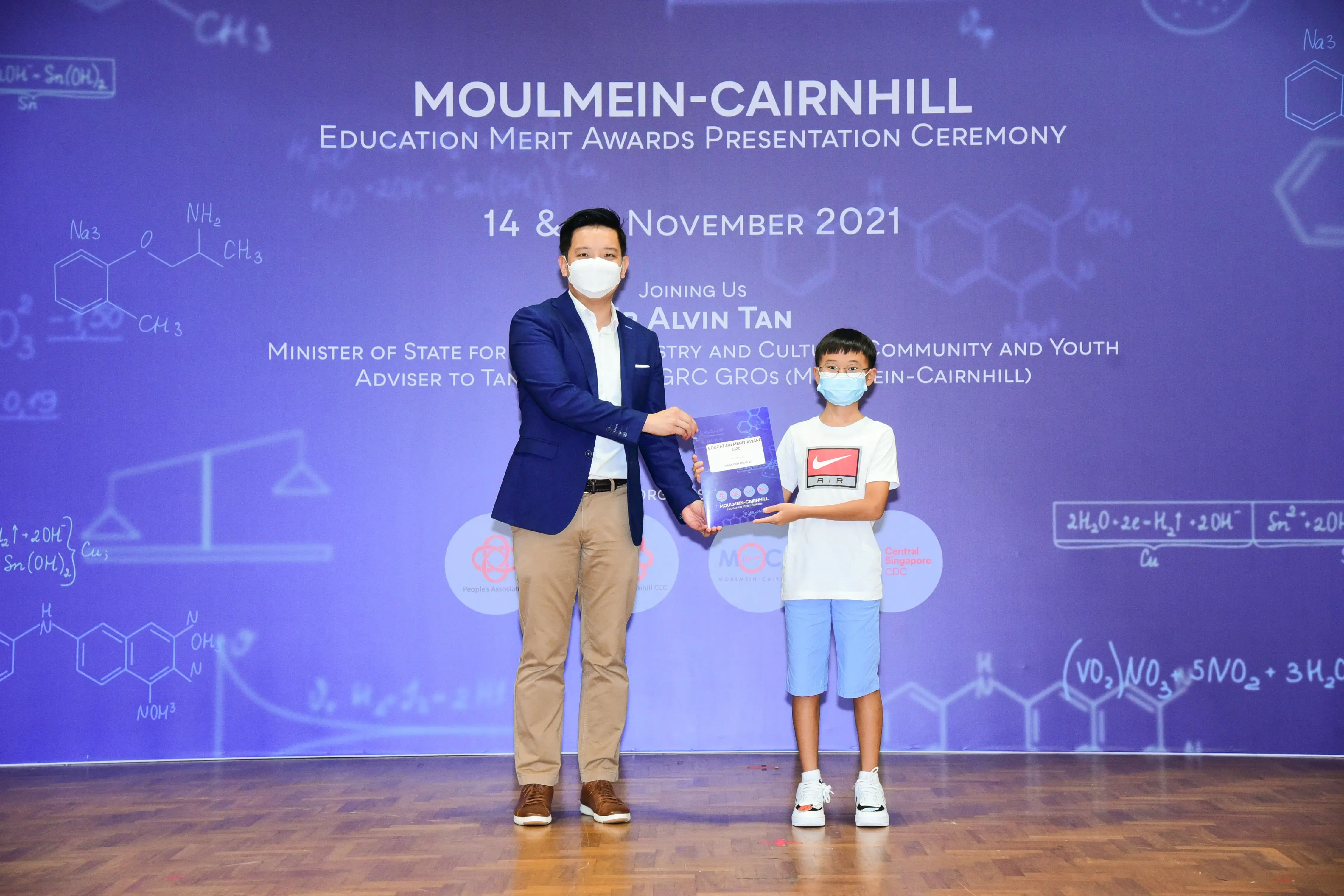 An adult in a blue blazer presents an award to a young boy at the Moulmein-Cairnhill Education Merit Awards 2021.