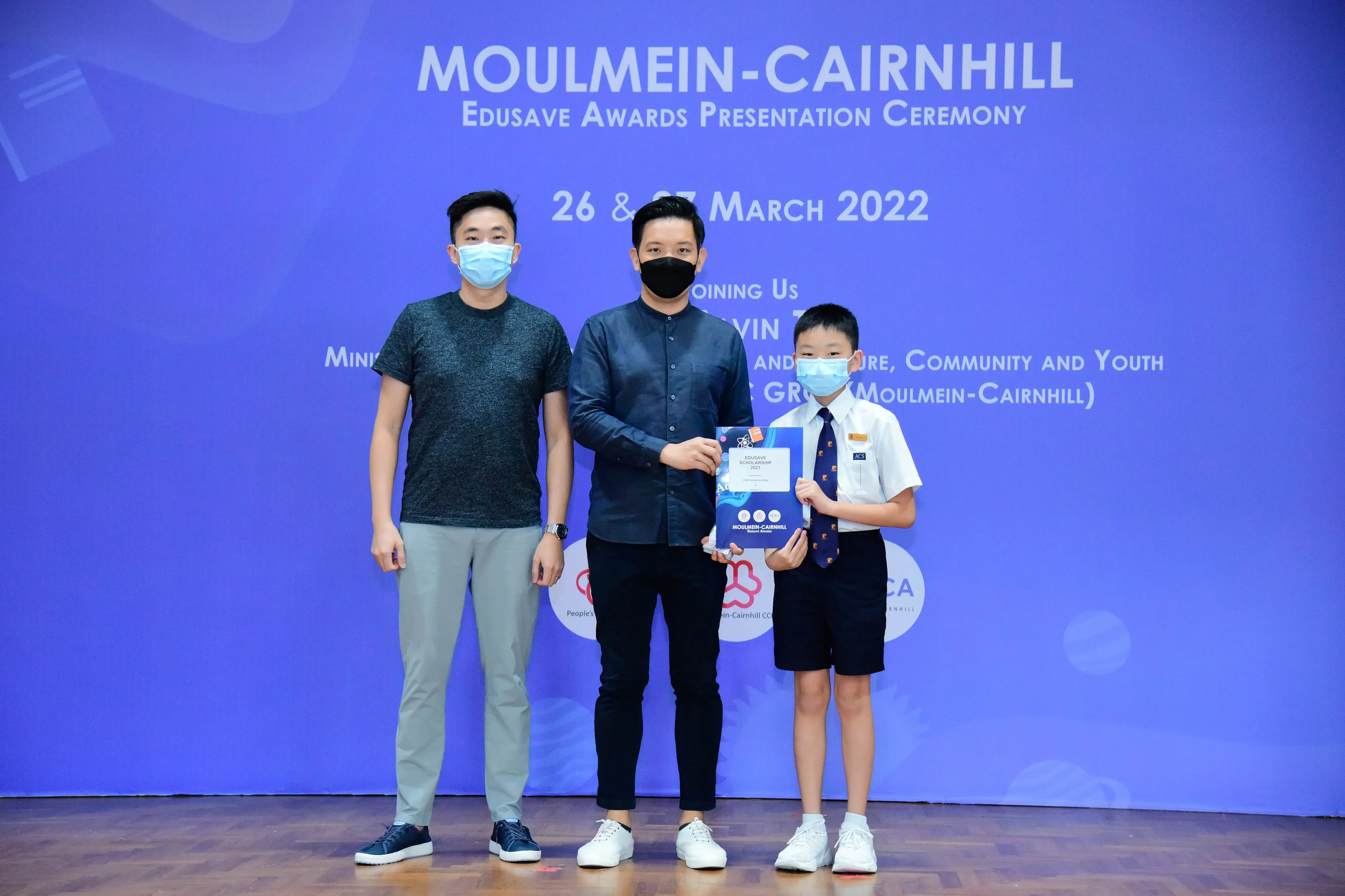 Two masked adults and a masked young boy pose at the Moulmein-Cairnhill Edusave Awards Ceremony, March 2022.