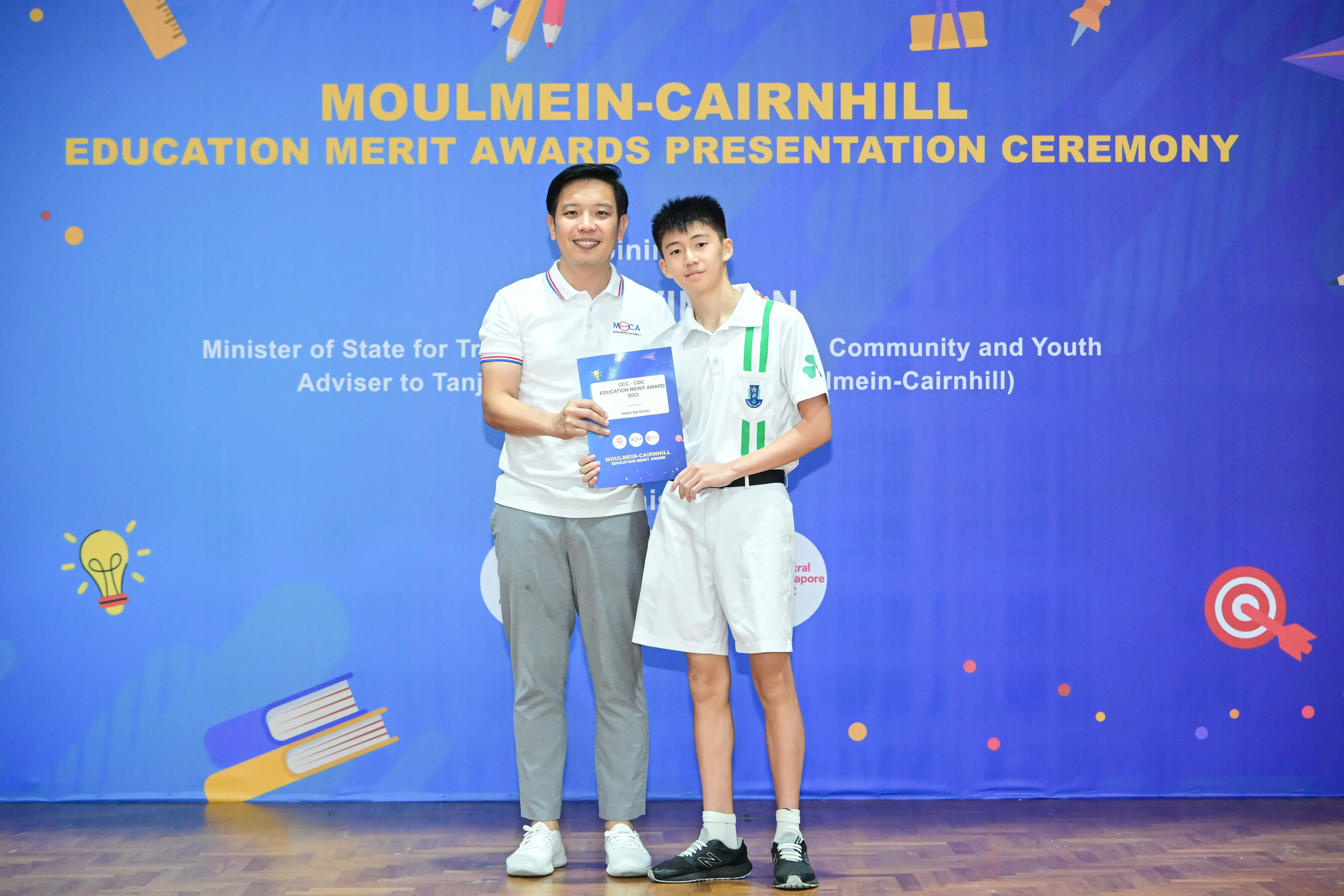 Two people pose holding an award booklet at the Moulmein-Cairnhill Education Merit Awards Presentation Ceremony.