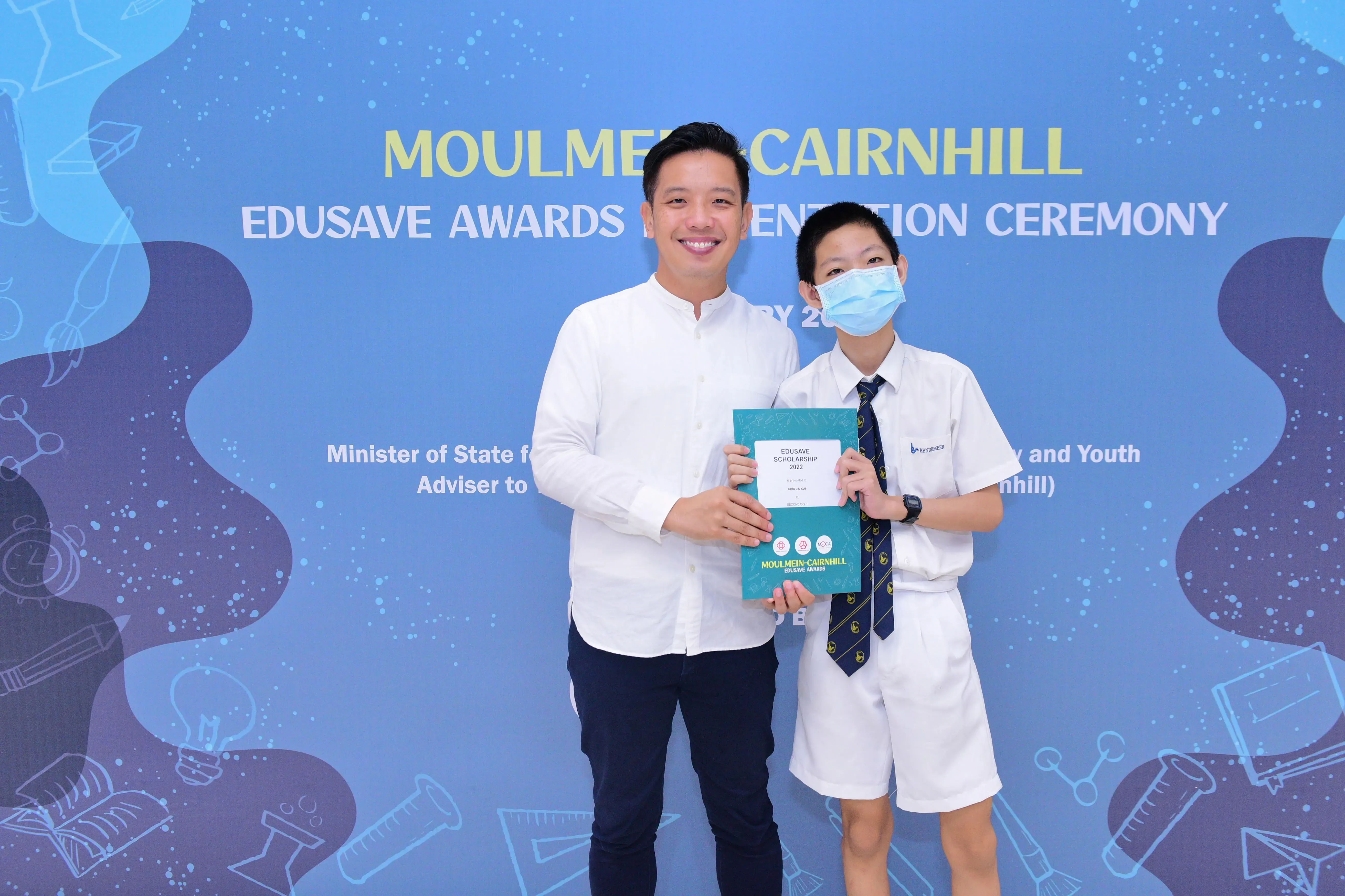 A man and a masked student hold an Edusave Scholarship certificate at the Moulmein-Cairnhill Edusave Awards Ceremony.