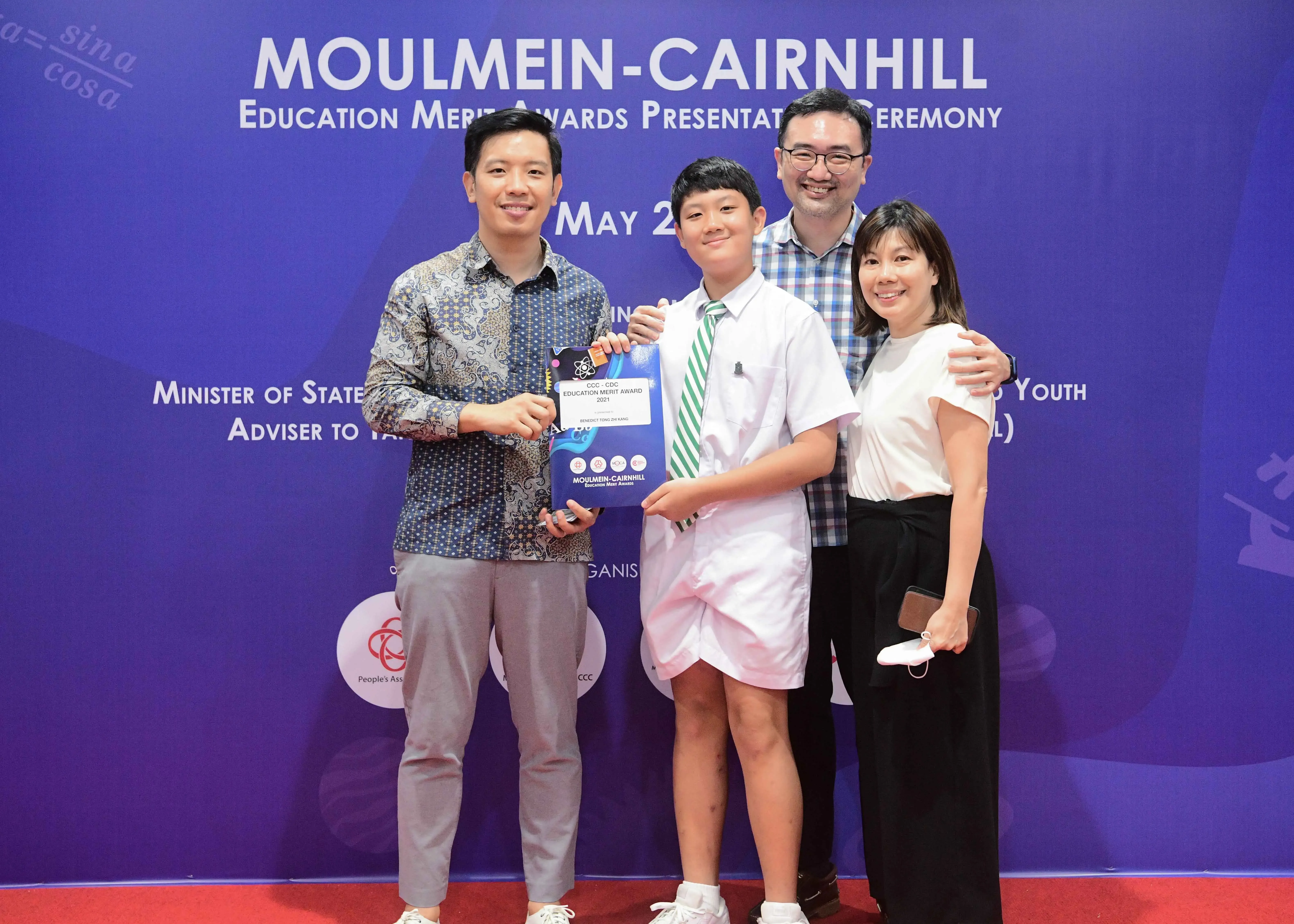 Four people pose at the Moulmein-Cairnhill Education Merit Awards ceremony, with a student holding an award certificate.