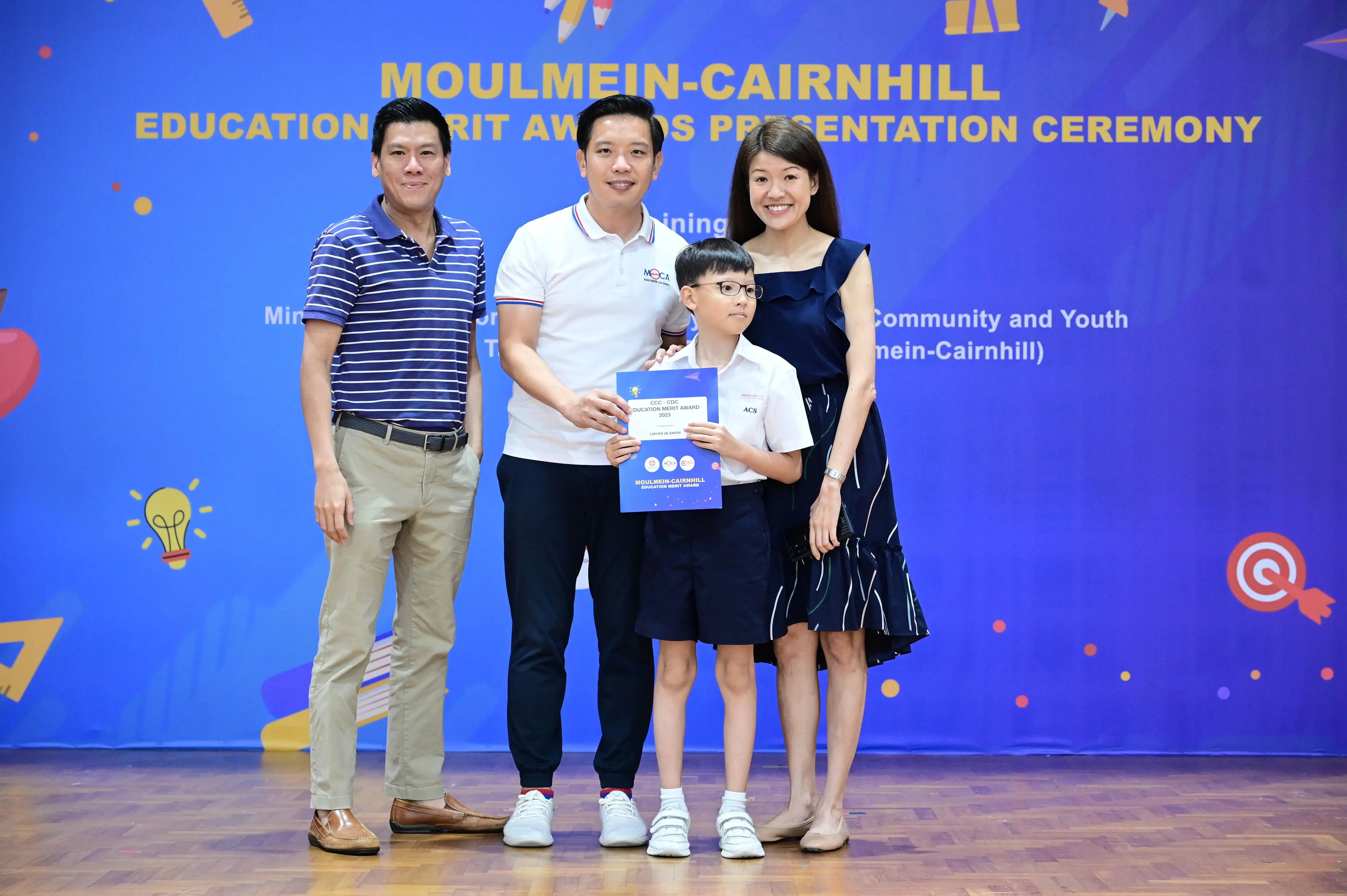 Three adults and a young boy holding a certificate at the Moulmein-Cairnhill Education Merit Awards ceremony.