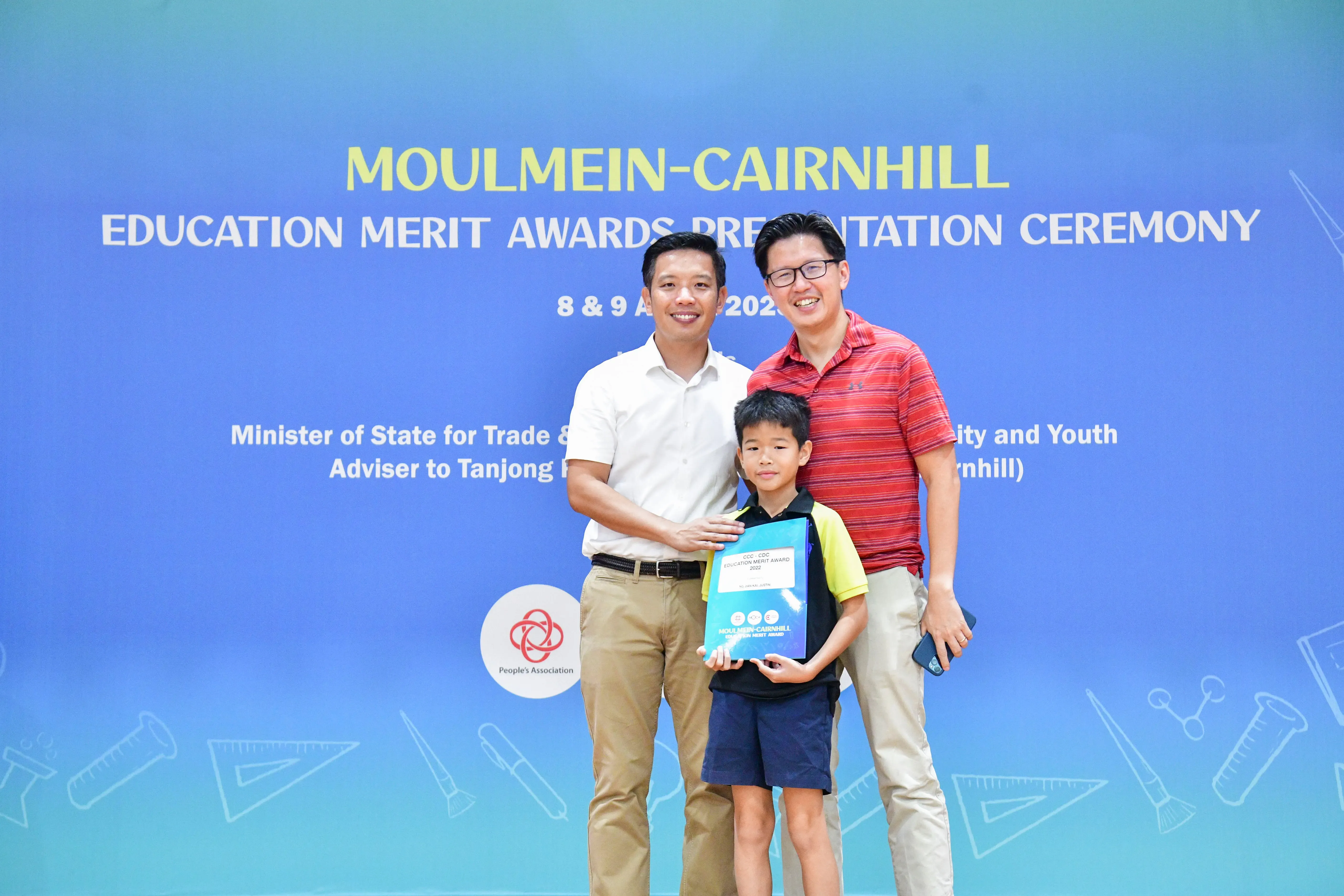 Two men and a young boy pose at the Moulmein-Cairnhill Education Merit Awards Presentation Ceremony backdrop.