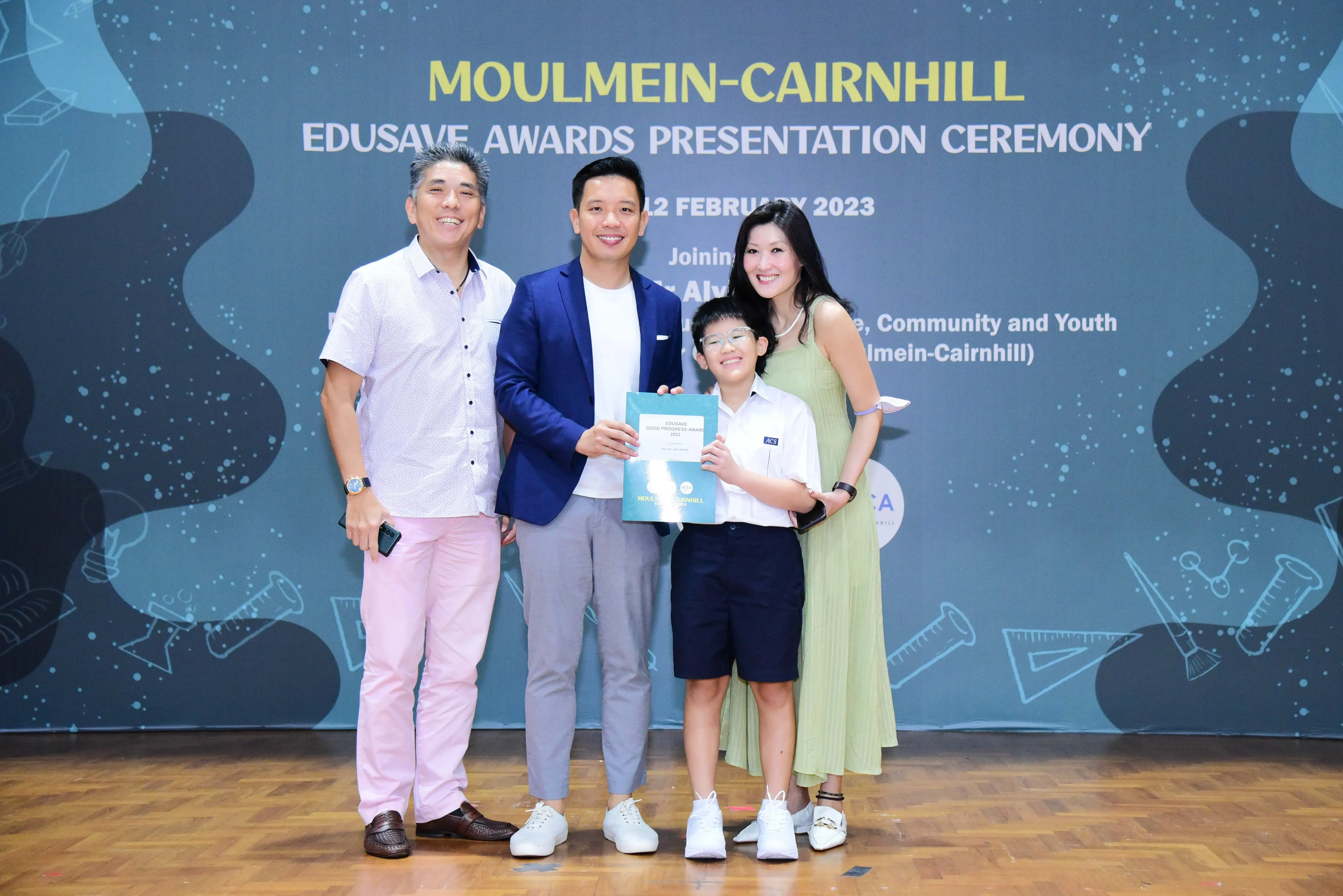 Four people pose at the Moulmein-Cairnhill Edusave Awards Presentation Ceremony in February 2023, with a boy holding a certificate.