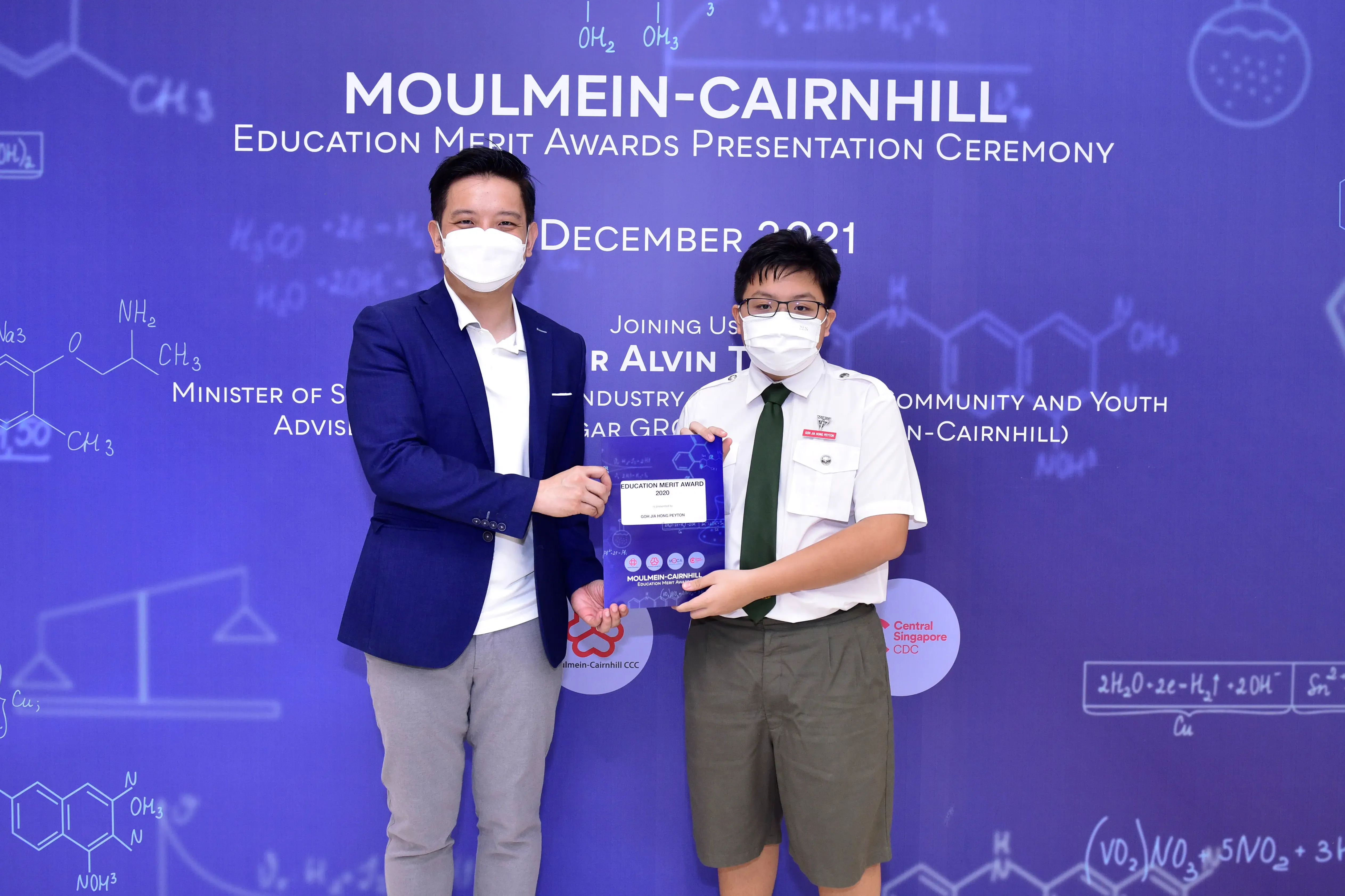 Two masked individuals hold an award certificate at the Moulmein-Cairnhill Education Merit Awards Ceremony, December 2021.